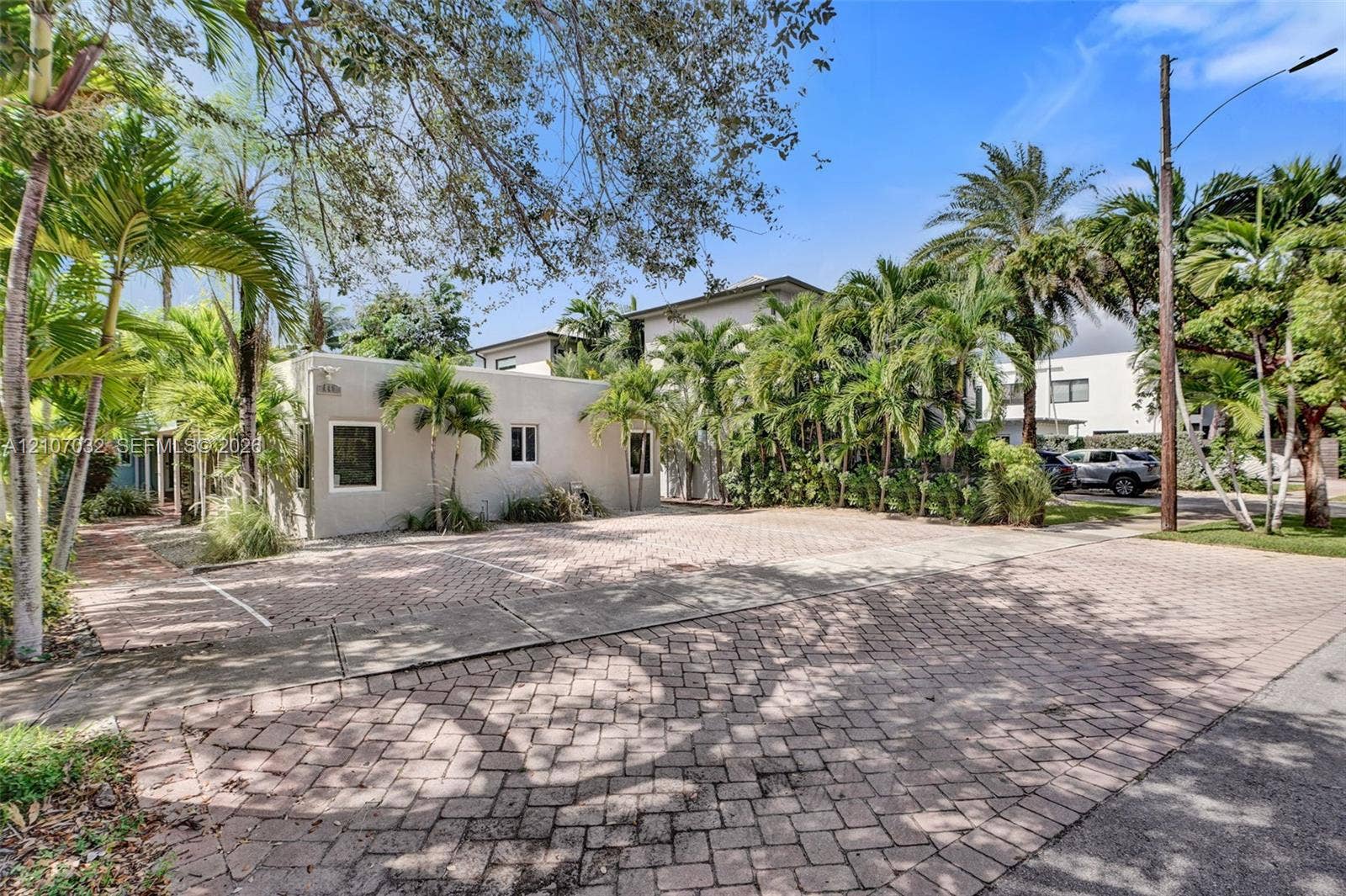443 NE 17th Way, Fort Lauderdale, FL 33301 Exterior of the property featuring a paver driveway, light-toned stucco siding, and mature palm landscaping