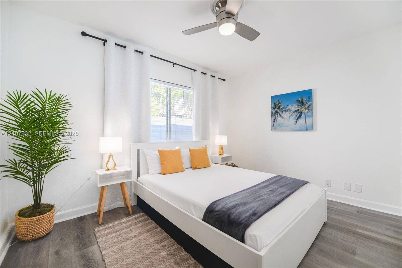 443 NE 17th Way, Fort Lauderdale, FL 33301 Neutral-toned bedroom featuring wood-finish flooring, a brushed metal ceiling fan with integrated lighting, and a single window framed by an adjustable curtain rod