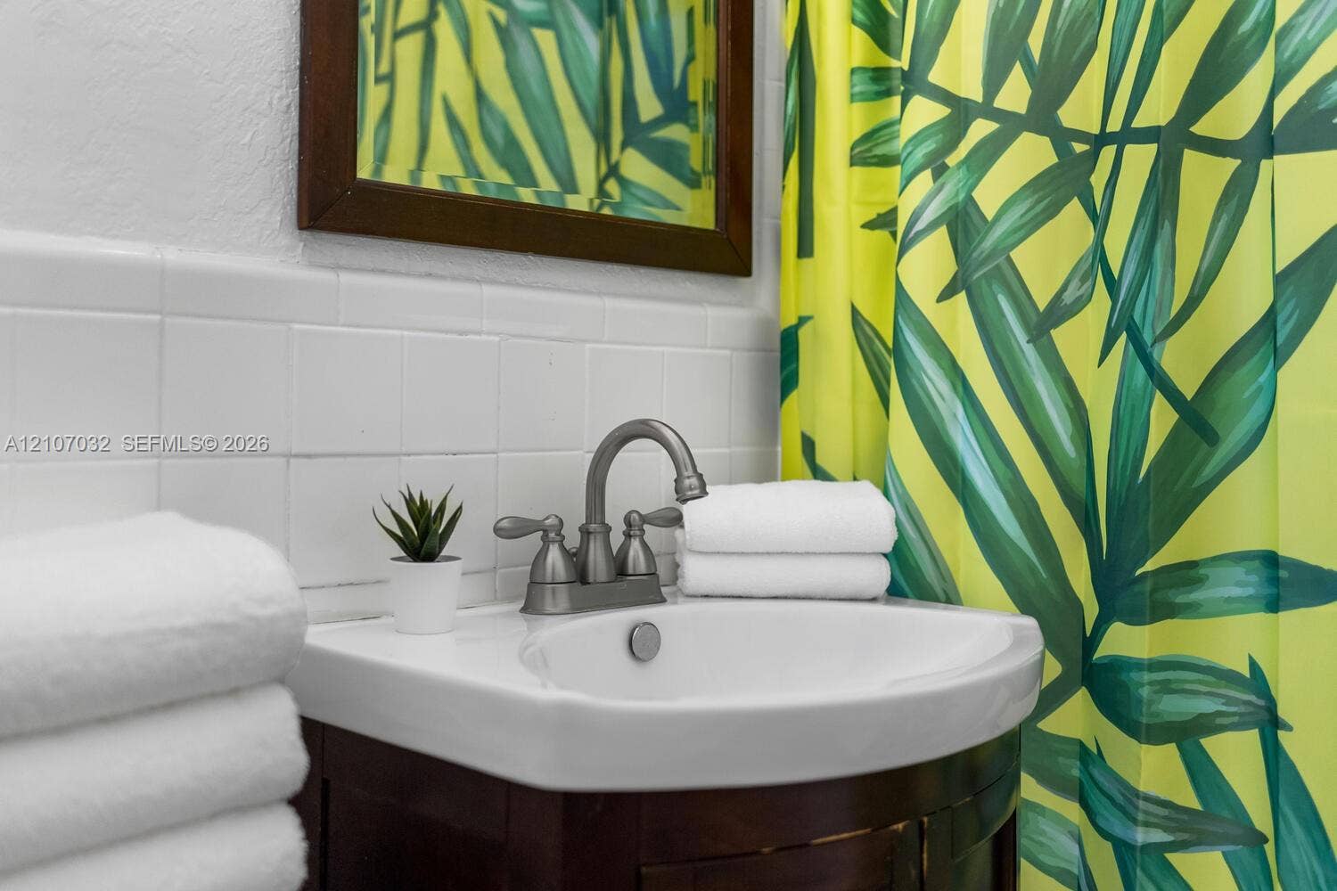 443 NE 17th Way, Fort Lauderdale, FL 33301 Curved wood-finish vanity featuring an integrated basin, brushed nickel dual-handle faucet, white tile backsplash, and a framed mirror