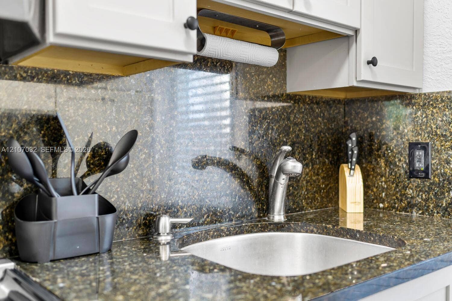 443 NE 17th Way, Fort Lauderdale, FL 33301 Polished stone countertop and matching full-height backsplash, undermount stainless steel sink, pull-down chrome faucet, and shaker-style cabinetry with matte black hardware