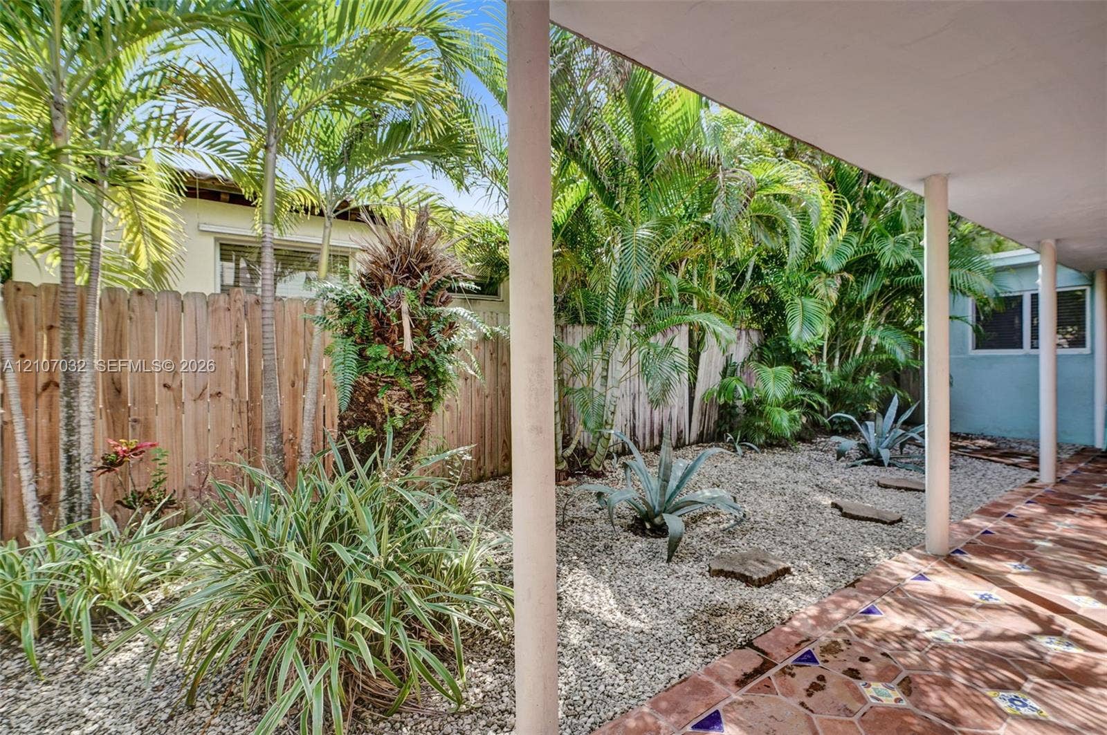 443 NE 17th Way, Fort Lauderdale, FL 33301 Covered patio featuring decorative tile flooring, gravel landscaping, established palms, and a wood privacy fence