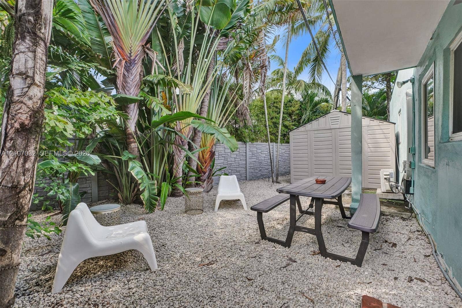 443 NE 17th Way, Fort Lauderdale, FL 33301 Private outdoor space featuring gravel ground cover, mature tropical landscaping, a perimeter wall, and an exterior storage structure
