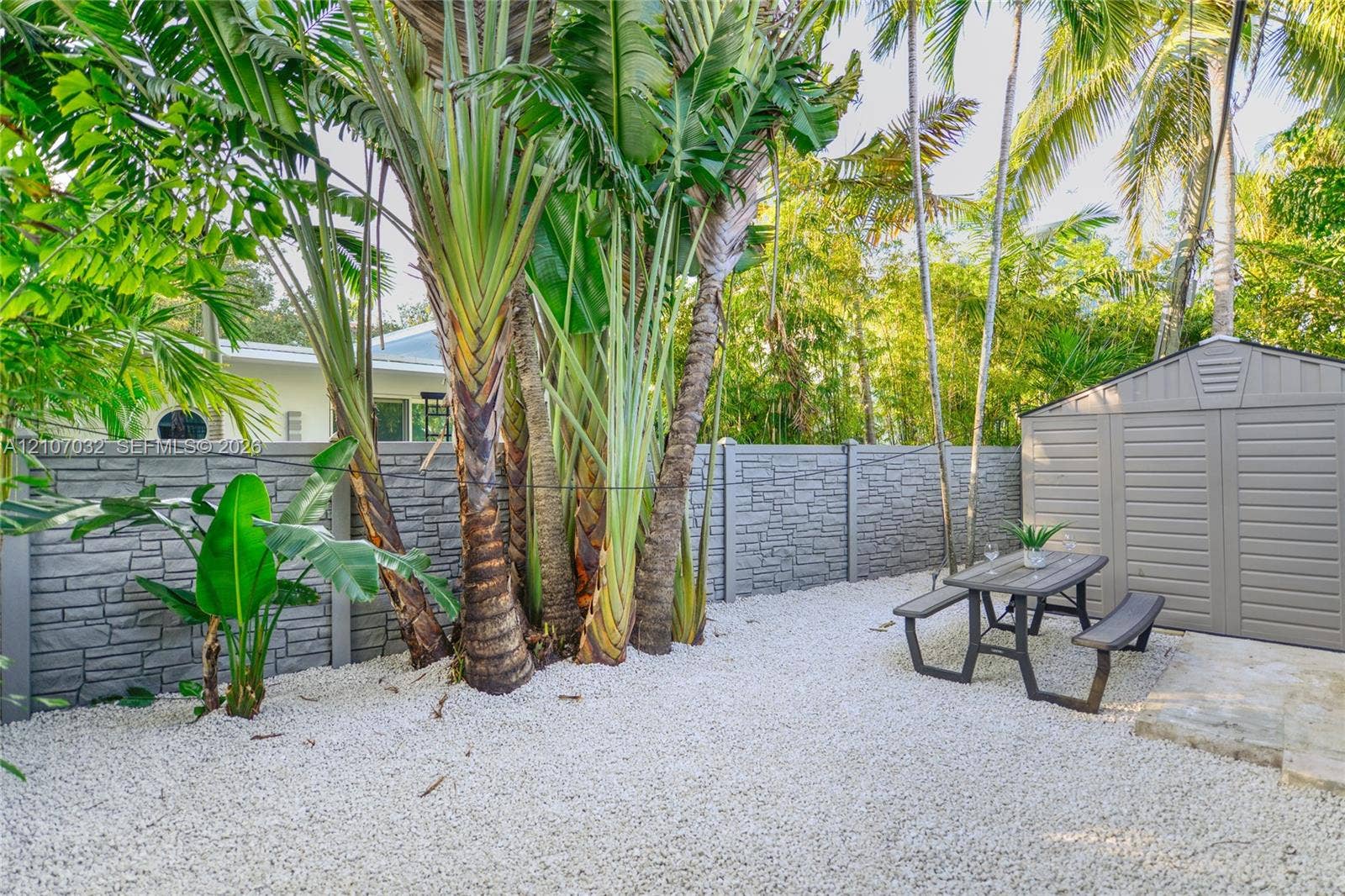 443 NE 17th Way, Fort Lauderdale, FL 33301 Outdoor space featuring a grey stone-patterned fence, white gravel ground cover, mature palm trees, and a detached storage shed