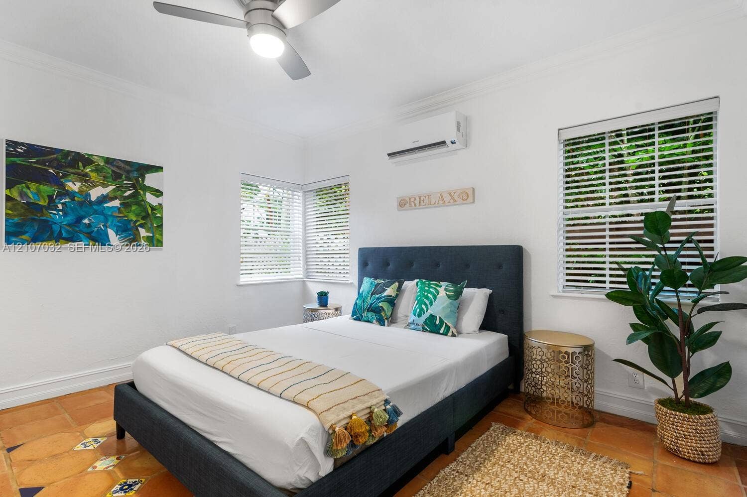 443 NE 17th Way, Fort Lauderdale, FL 33301 Neutral-toned room featuring terra-cotta tile flooring, a wall-mounted ductless air conditioning unit, a ceiling fan with integrated lighting, and multiple windows with horizontal blinds