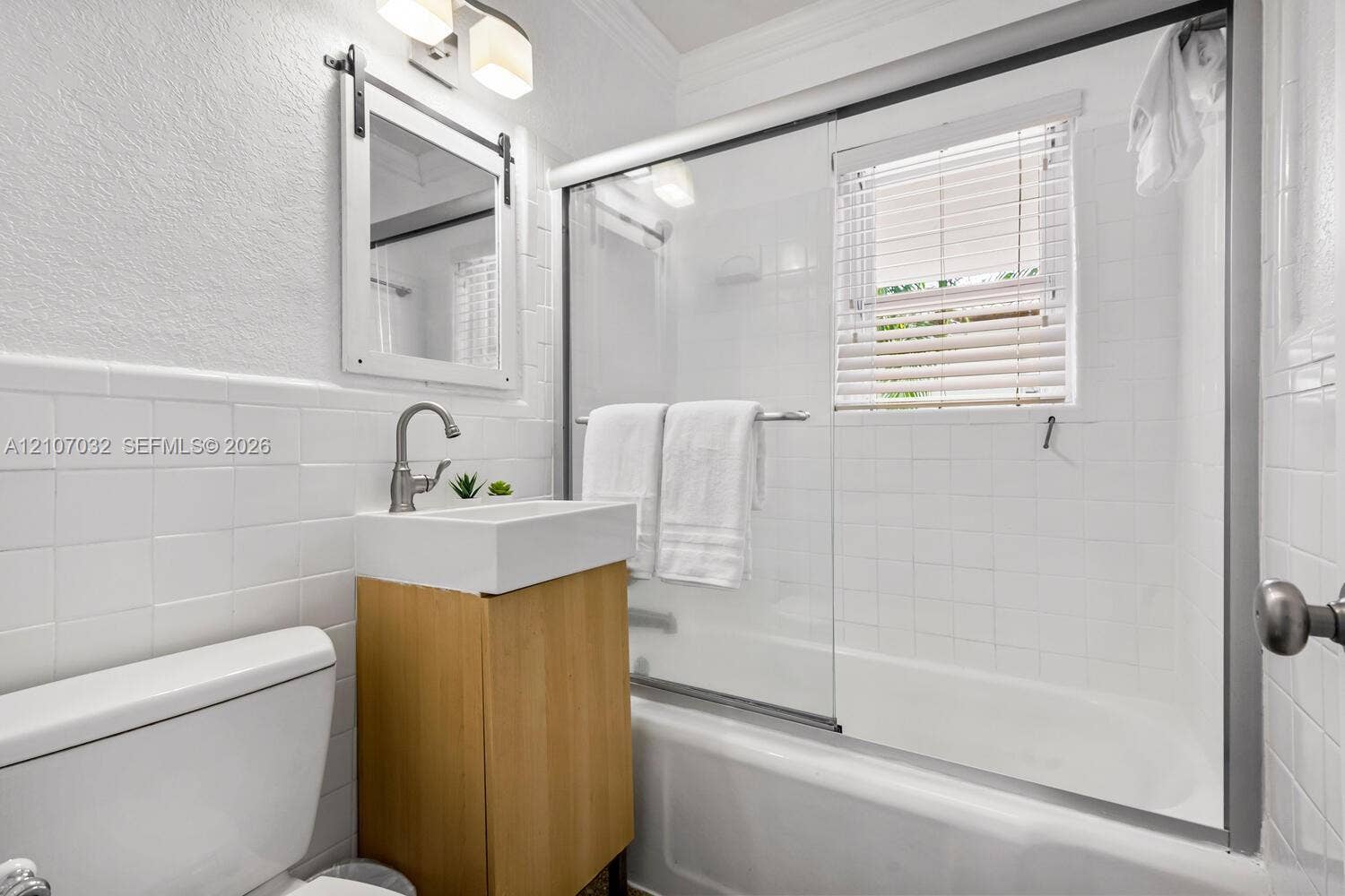 443 NE 17th Way, Fort Lauderdale, FL 33301 Bathroom featuring a vanity with a rectangular vessel sink, sliding glass shower doors, subway-style wall tile, a barn-door style framed mirror, and a wall-mounted light fixture