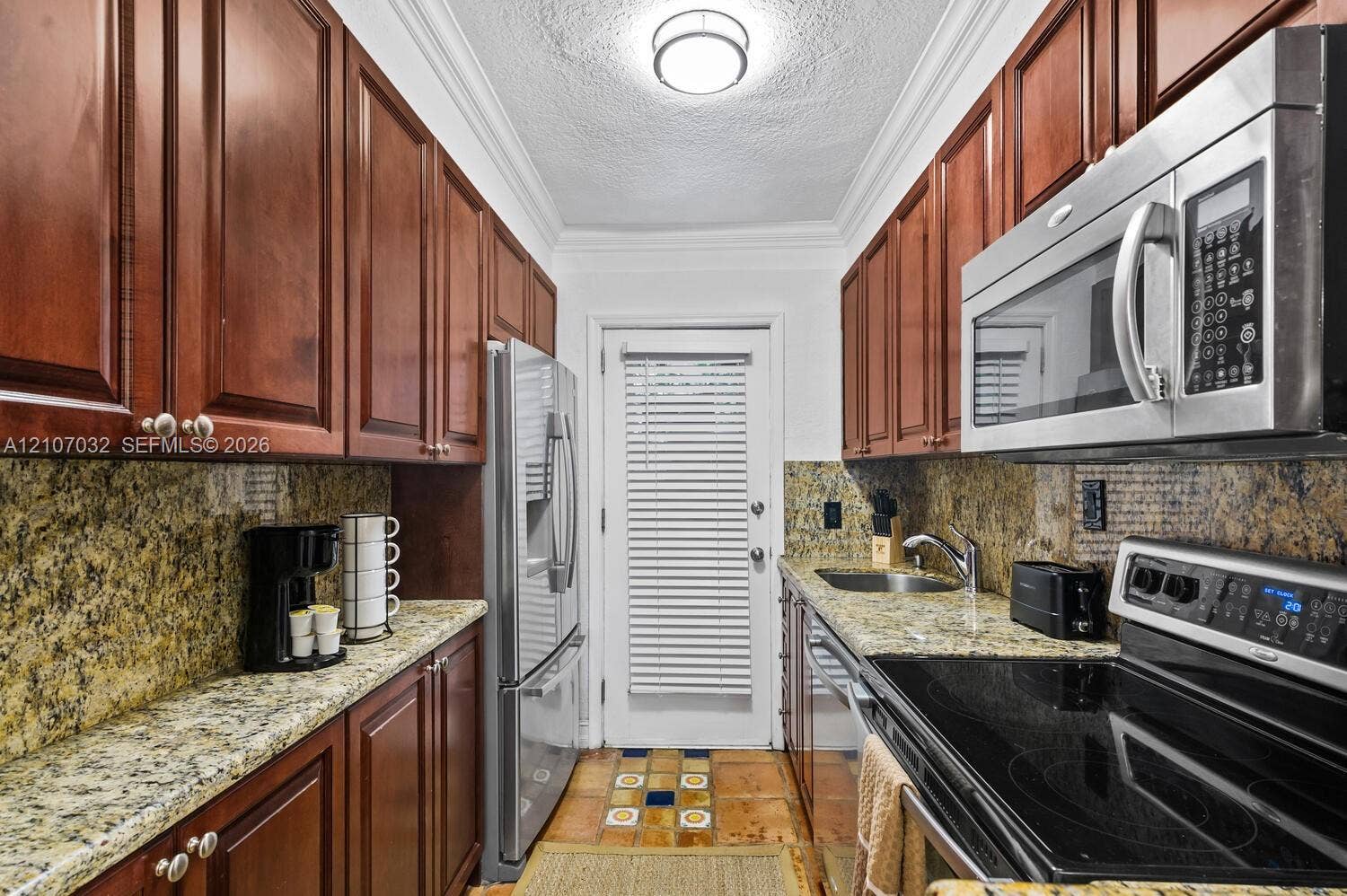 443 NE 17th Way, Fort Lauderdale, FL 33301 Galley kitchen featuring rich-toned wood cabinetry, stone countertops, stainless steel appliances, and tile flooring