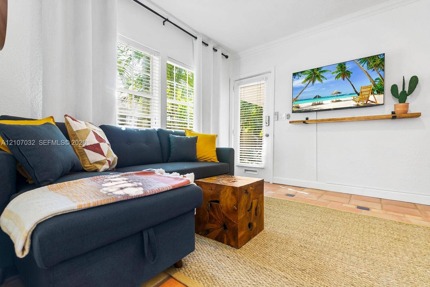 443 NE 17th Way, Fort Lauderdale, FL 33301 Bright living area featuring tile flooring, crown molding, double windows with blinds, and a built-in wall-mounted wooden shelf
