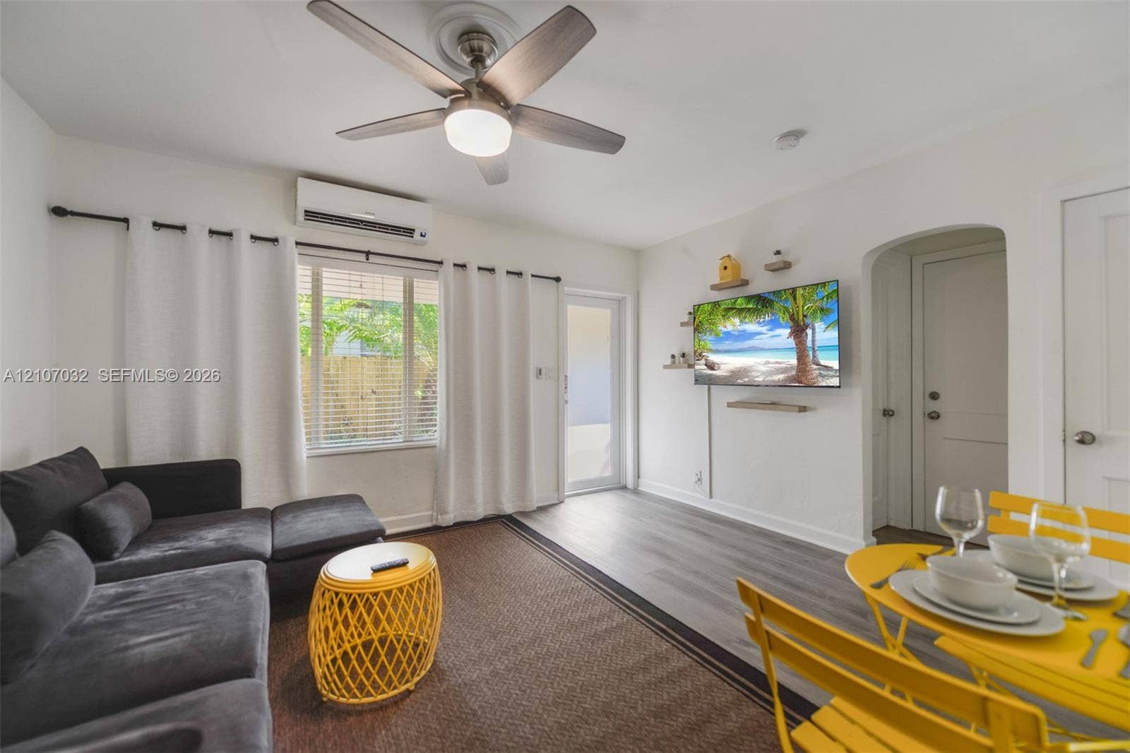 443 NE 17th Way, Fort Lauderdale, FL 33301 Neutral-toned wood-finish flooring, wall-mounted ductless mini-split HVAC unit, ceiling fan with integrated lighting, and an arched doorway
