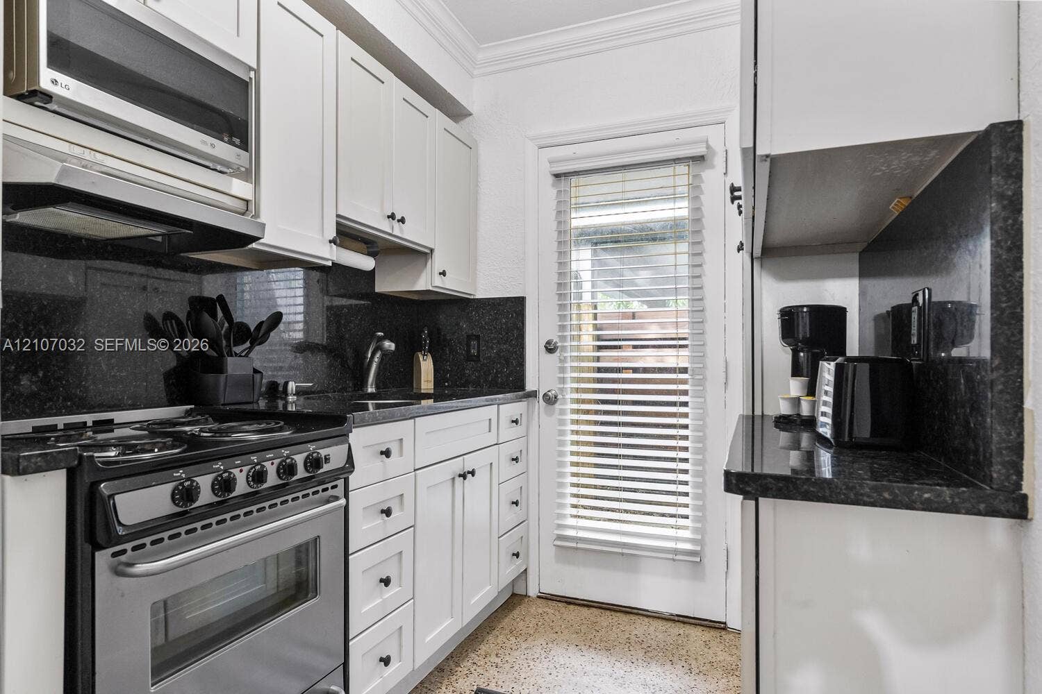 443 NE 17th Way, Fort Lauderdale, FL 33301 Kitchen featuring white Shaker-style cabinetry, dark stone countertops, matching full-height stone backsplash, integrated stainless steel gas range, and speckled hard-surface flooring