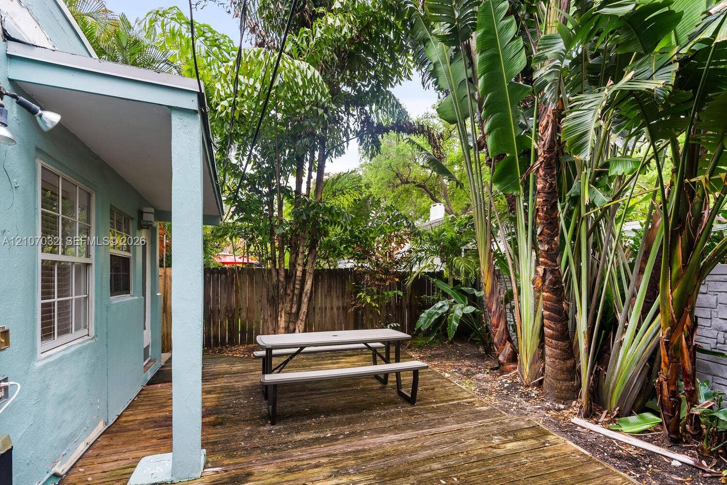 443 NE 17th Way, Fort Lauderdale, FL 33301 Wood-plank patio deck featuring a covered porch overhang, privacy wood fencing, and mature tropical landscaping