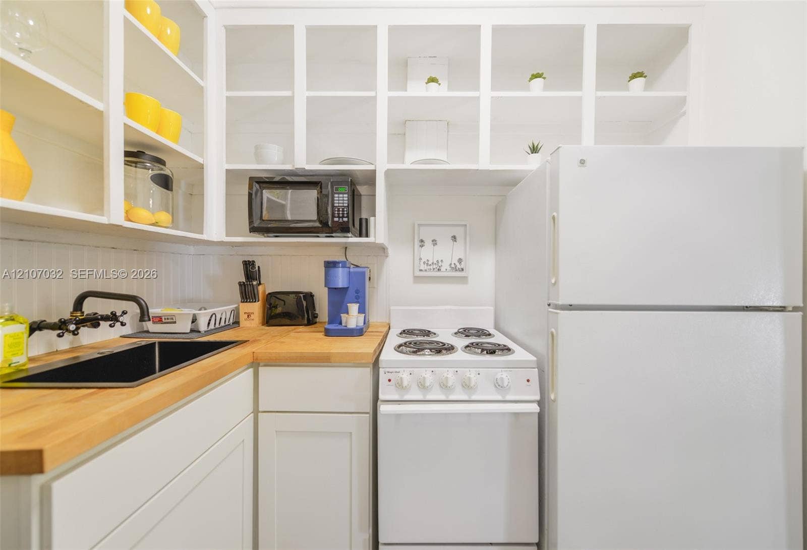 443 NE 17th Way, Fort Lauderdale, FL 33301 Kitchen featuring white cabinetry with open shelving, wood-finish countertops, an undermount sink with a matte black faucet, and white appliances