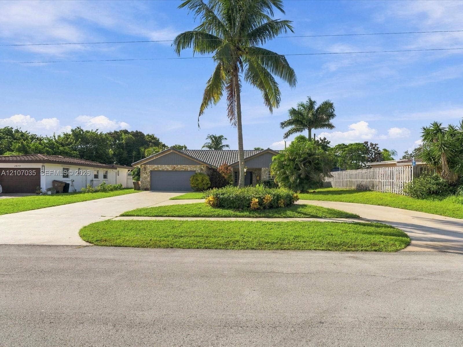 1006 SE 6th Street, Deerfield Beach, FL 33441 featuring a stone facade, multi-car garage, circular concrete driveway, and mature landscaping