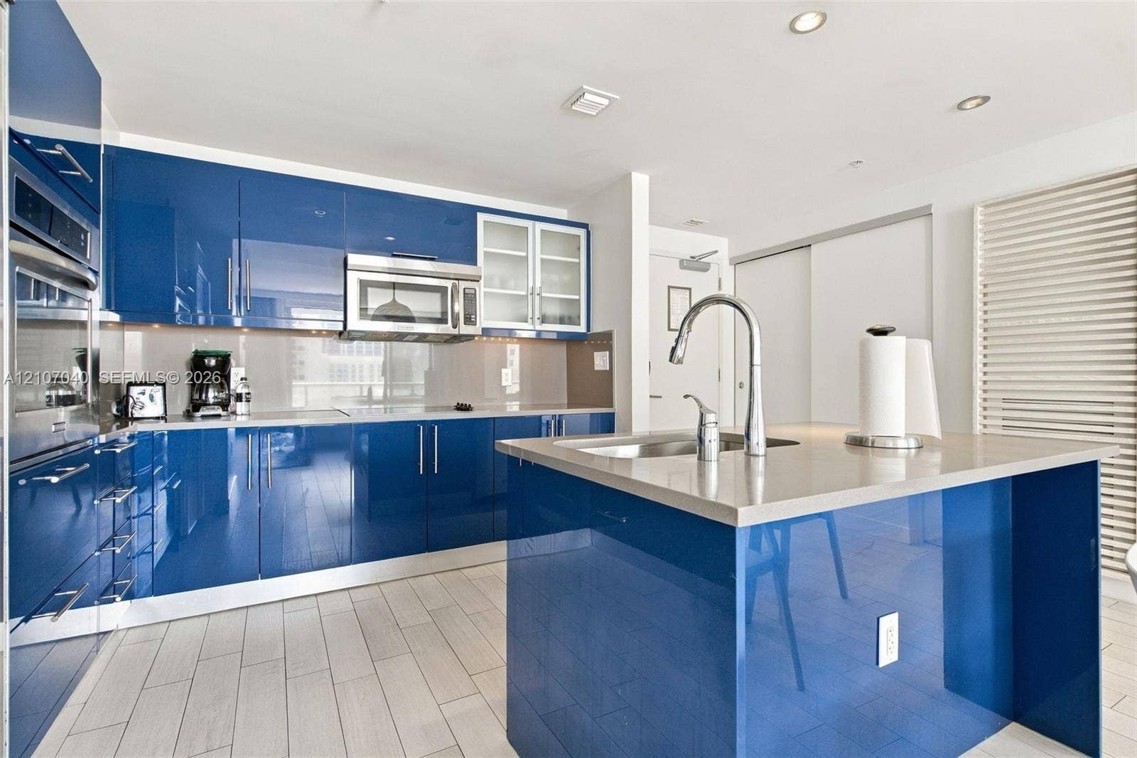 3101 Bayshore Drive, #707, Fort Lauderdale, FL 33304 Glossy blue cabinetry, solid surface countertops, center island with an integrated sink, stainless steel microwave, and wood-finish tile flooring
