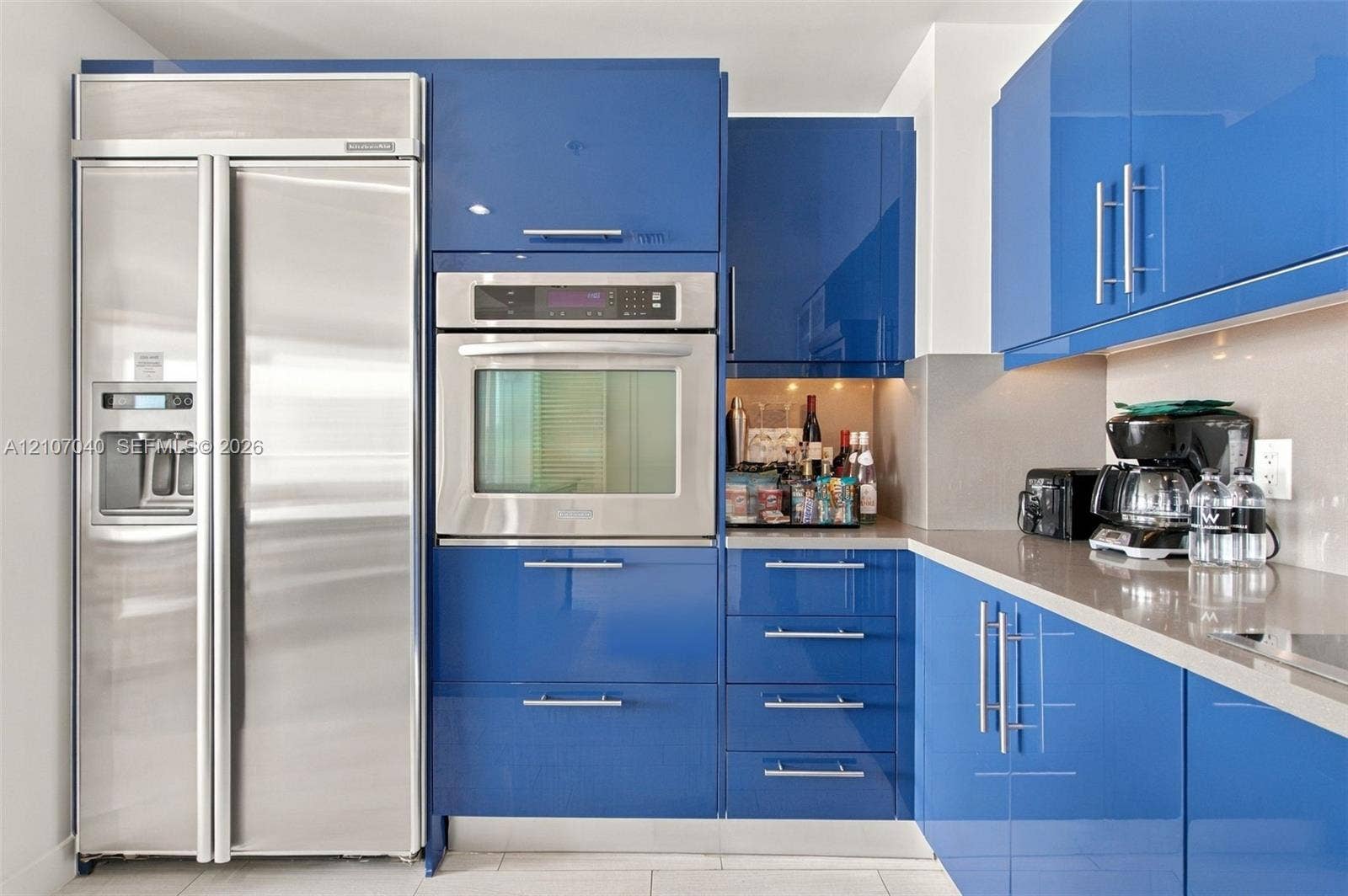 3101 Bayshore Drive, #707, Fort Lauderdale, FL 33304 Kitchen featuring high-gloss blue cabinetry with polished metal hardware, integrated stainless steel side-by-side refrigerator, built-in wall oven, and neutral solid-surface countertops