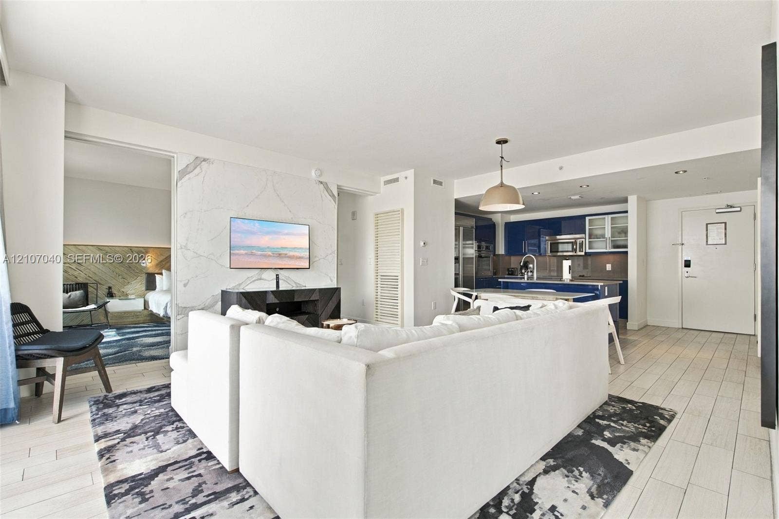 3101 Bayshore Drive, #707, Fort Lauderdale, FL 33304 Open-concept living space featuring large-format tile flooring, a floor-to-ceiling stone-surround wall, glossy navy cabinetry, integrated kitchen appliances, and a polished metal pendant light fixture