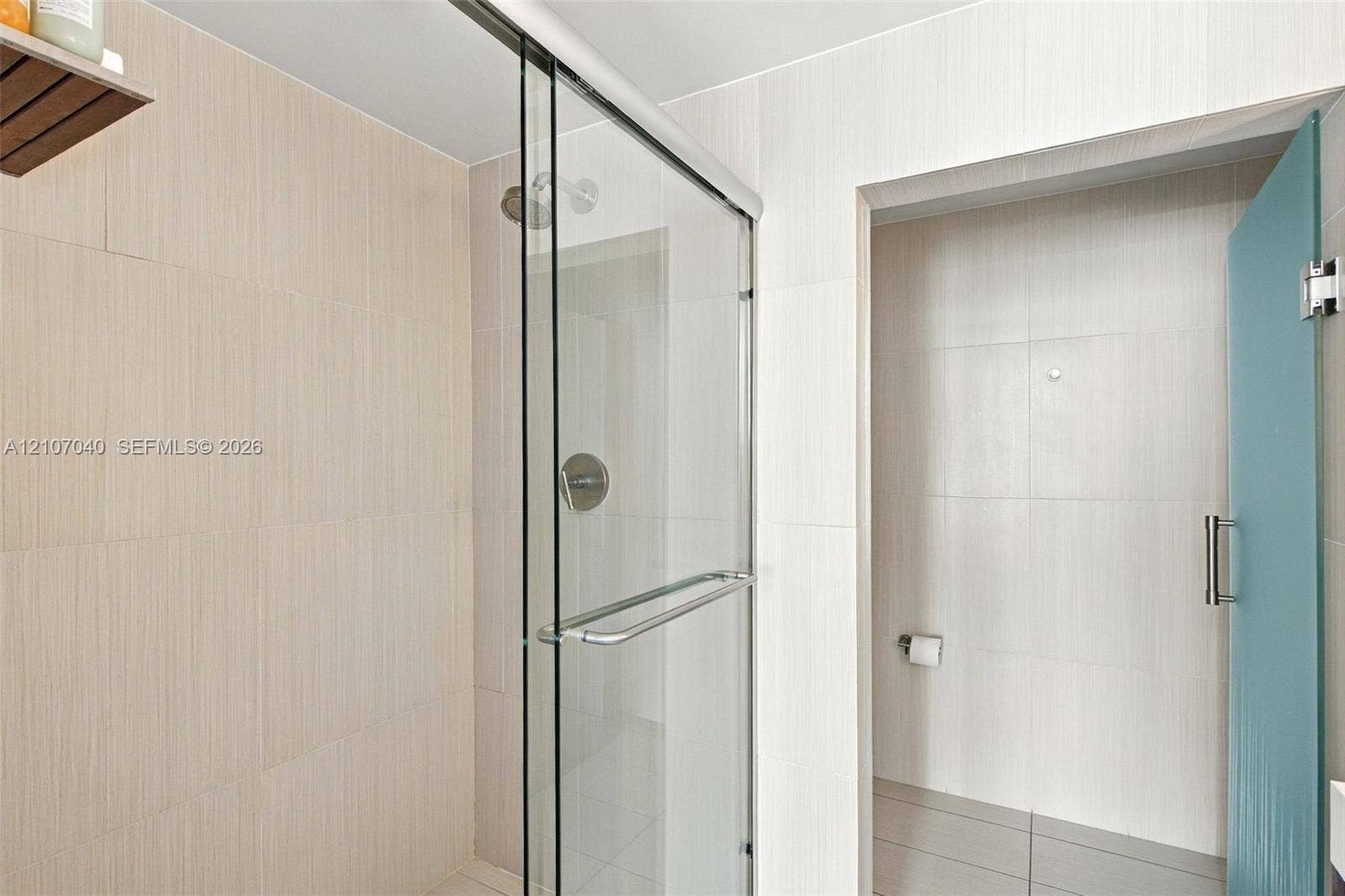 3101 Bayshore Drive, #707, Fort Lauderdale, FL 33304 Walk-in shower featuring floor-to-ceiling neutral tile, a frameless glass sliding door, polished chrome fixtures, and a glass-paneled entry door