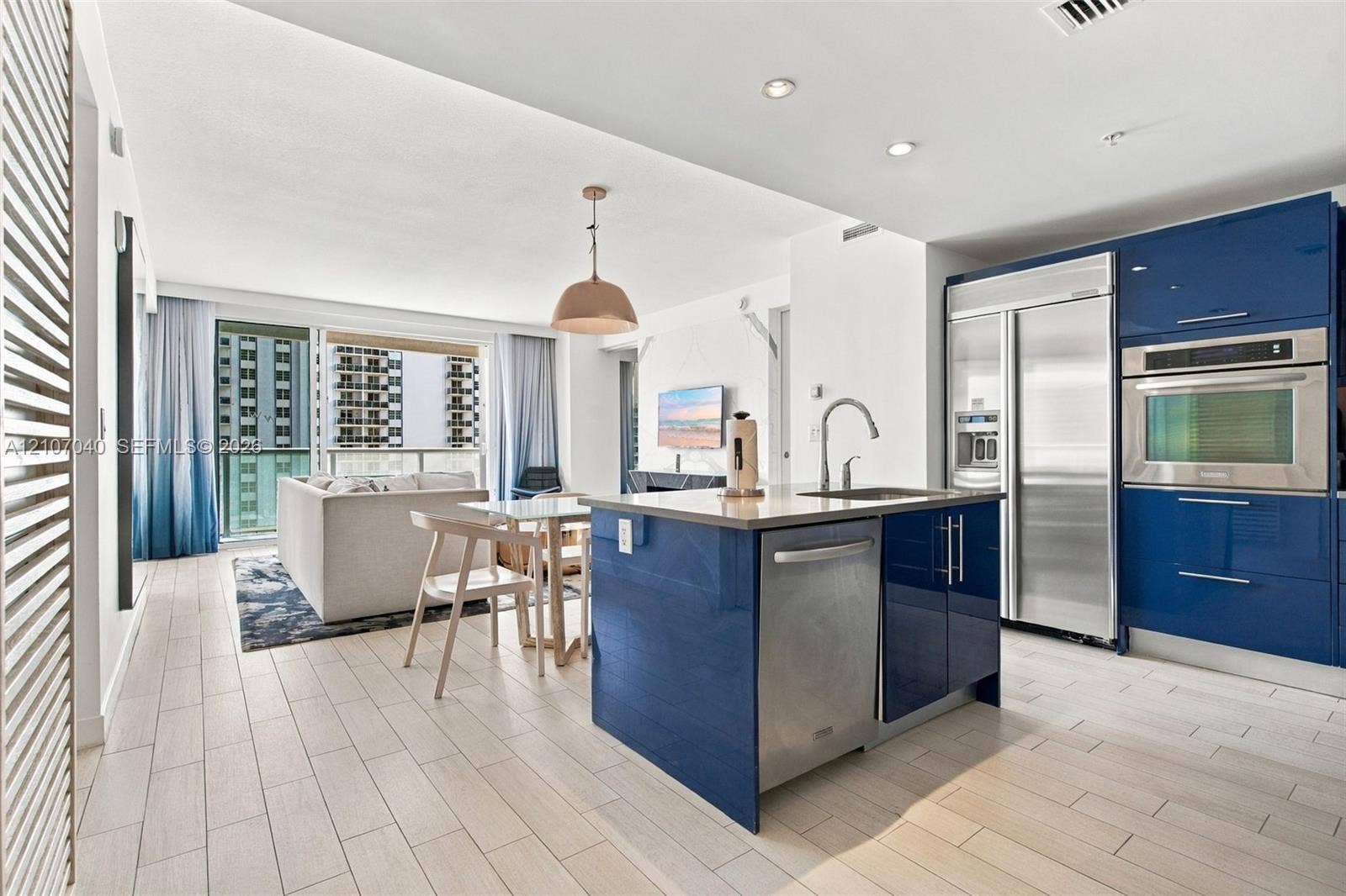 3101 Bayshore Drive, #707, Fort Lauderdale, FL 33304 Kitchen featuring high-gloss blue cabinetry, stainless steel appliances, a kitchen island with an undermount sink, and light-toned tile flooring