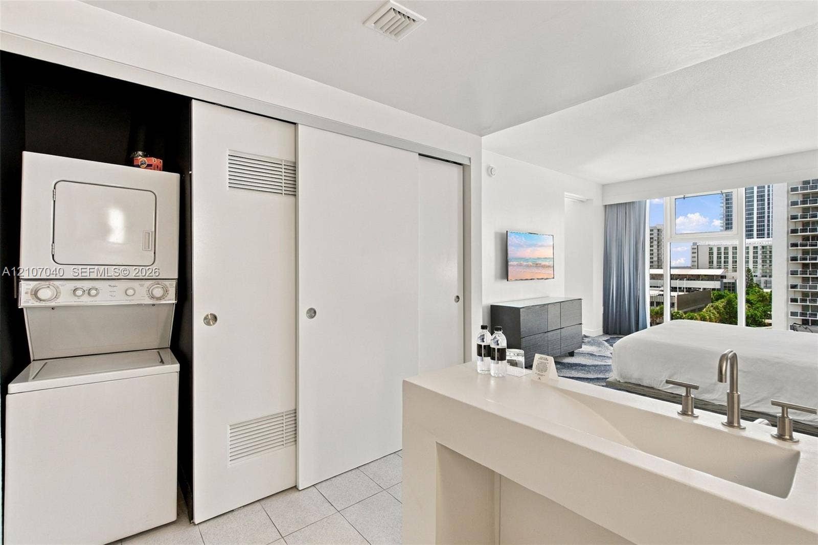 3101 Bayshore Drive, #707, Fort Lauderdale, FL 33304 Stacked washer and dryer unit, built-in floor-to-ceiling sliding closet doors, and custom white vanity with integrated basin and polished metal faucet