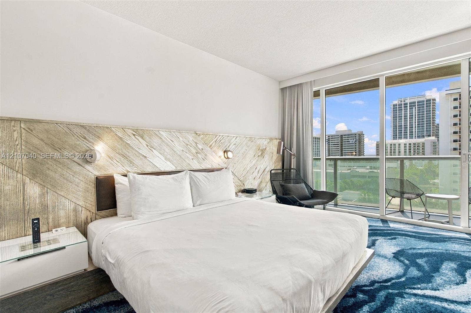 3101 Bayshore Drive, #707, Fort Lauderdale, FL 33304 Floor-to-ceiling glass sliding doors opening to a private balcony, custom wood-paneled accent wall, and wall-mounted reading lights