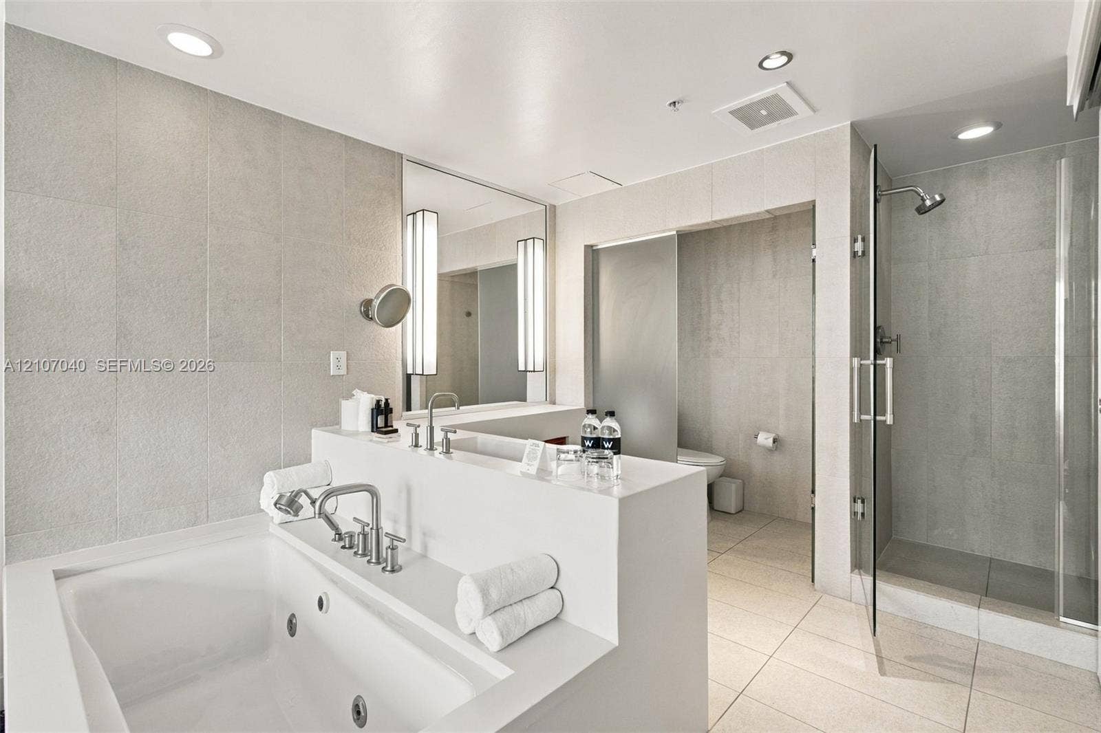 3101 Bayshore Drive, #707, Fort Lauderdale, FL 33304 Jetted soaking tub with polished chrome fixtures, walk-in glass-enclosed shower, large-format tile wall cladding, and recessed lighting