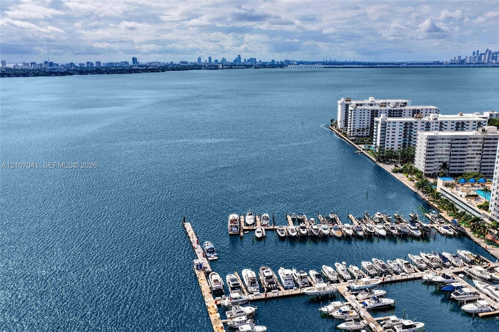 Waterfront aerial featuring a marina with multiple boat slips, deep-water access, and a panoramic urban skyline backdrop