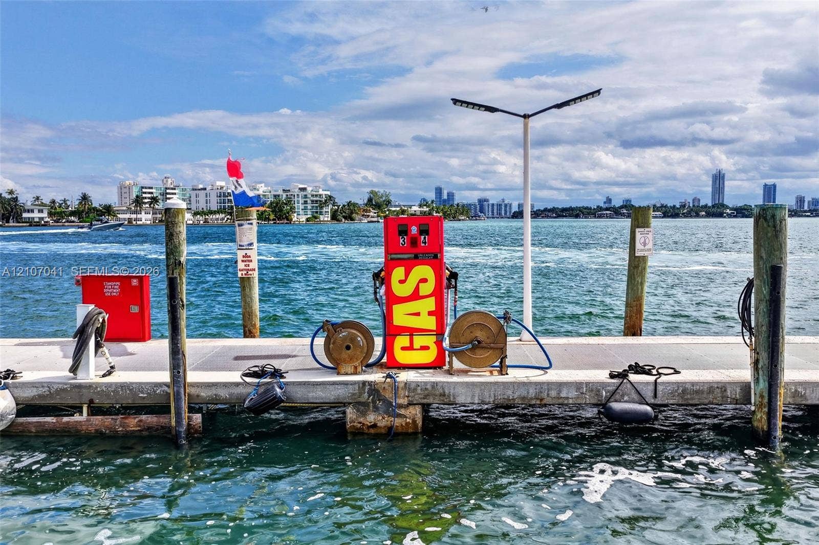 Concrete boat dock featuring a fuel dispensing station, dual hose reels, utility bollards, and overhead lighting