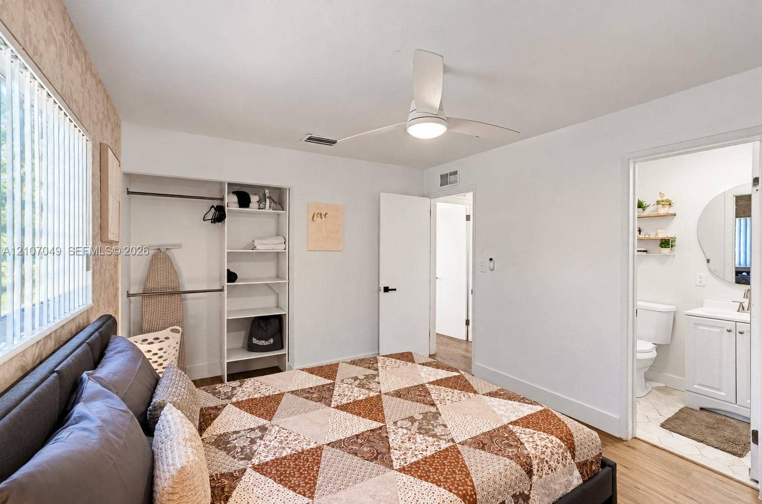 1009 NE 18th Street, Fort Lauderdale, FL 33305 Bedroom featuring wood-finish flooring, a ceiling fan with integrated lighting, a built-in closet system with open shelving, and a bathroom entry with a vanity and wall-mounted circular mirror