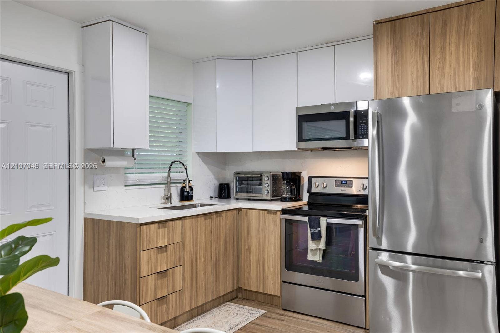 1009 NE 18th Street, Fort Lauderdale, FL 33305 Two-tone cabinetry featuring white upper and wood-finish lower cabinets, stainless steel appliances, white solid-surface countertops, and an undermount sink with a pull-down faucet