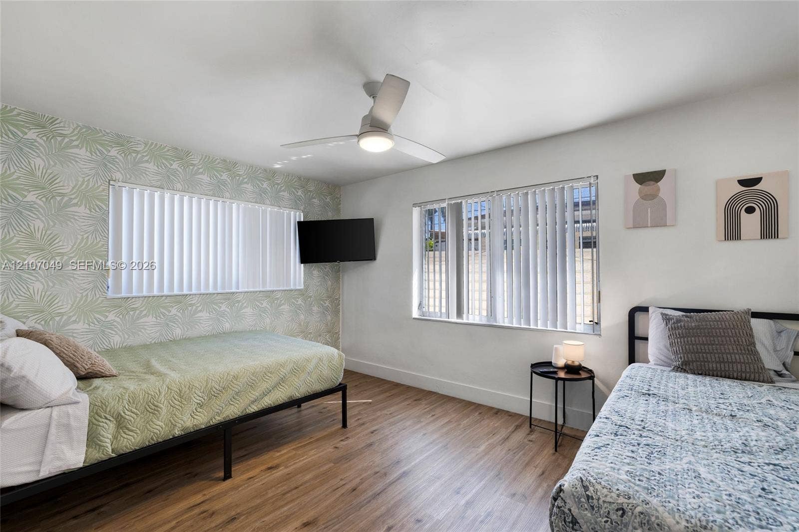 1009 NE 18th Street, Fort Lauderdale, FL 33305 Wood-finish flooring, patterned accent wall, and ceiling-mounted light fixture with integrated fan, featuring dual windows with vertical blinds