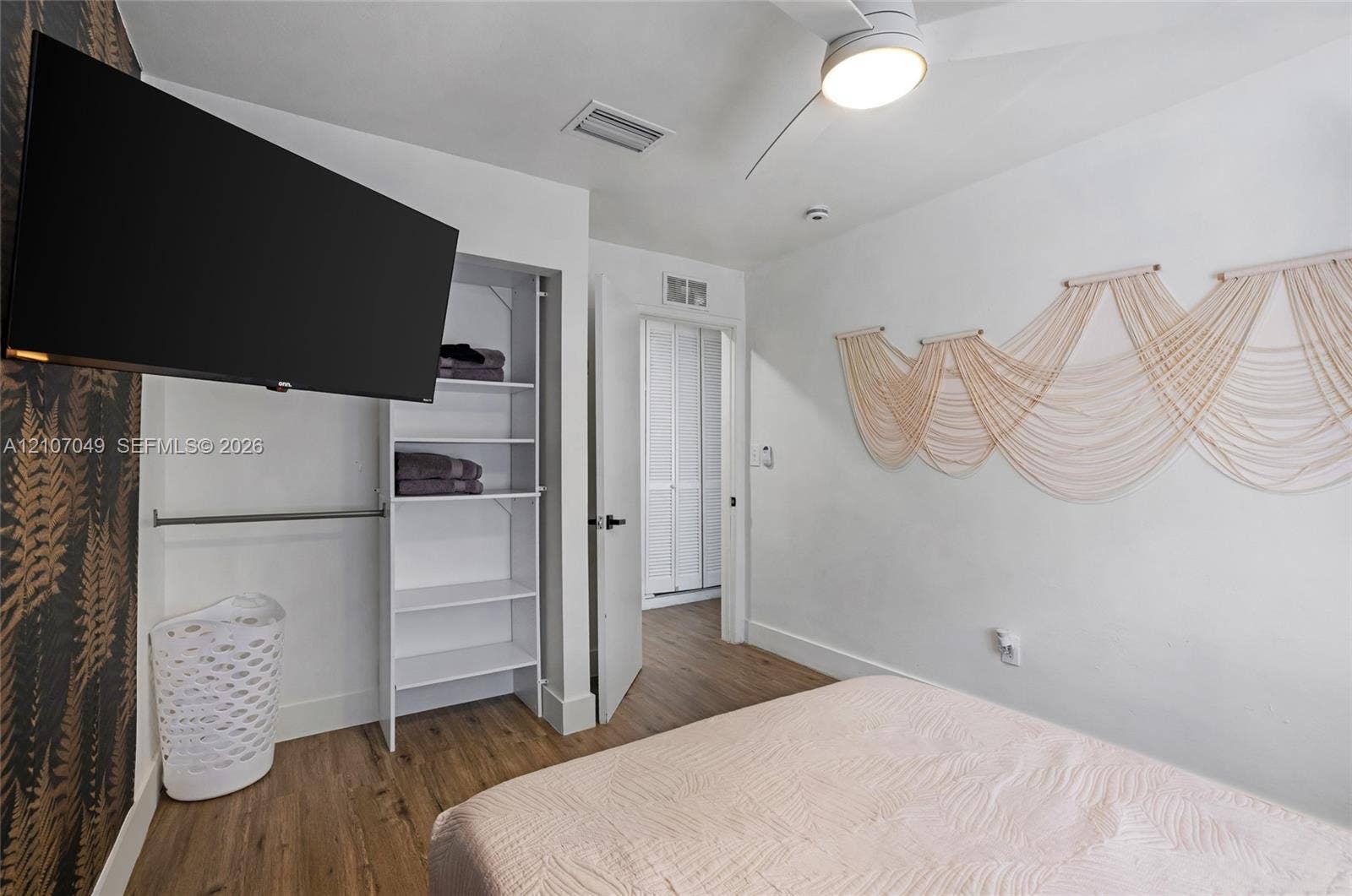 1009 NE 18th Street, Fort Lauderdale, FL 33305 Wood-finish flooring, accent wall with patterned wall covering, built-in open shelving, and a ceiling-mounted light fixture with integrated fan