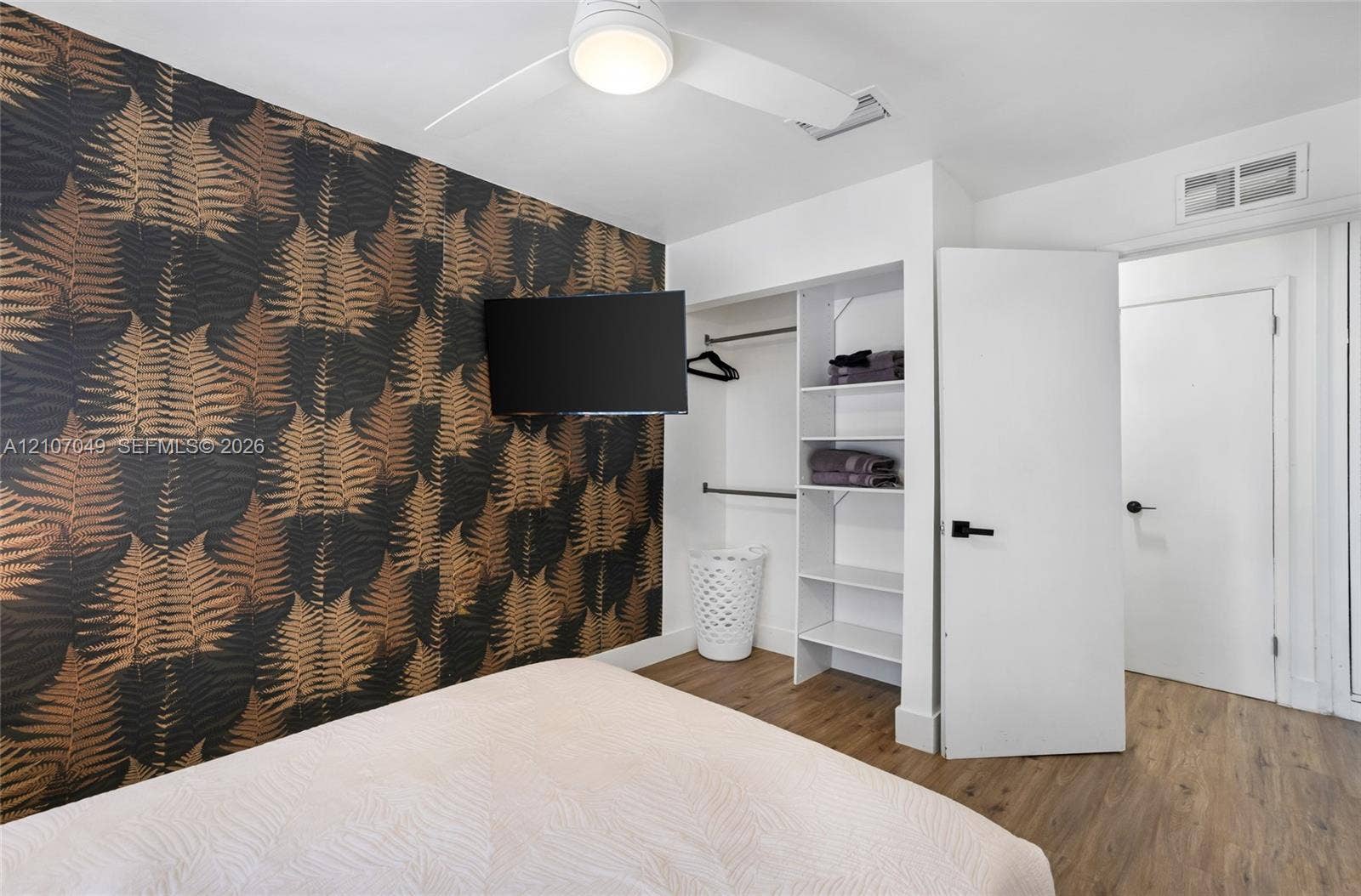 1009 NE 18th Street, Fort Lauderdale, FL 33305 Accent wall with botanical wallpaper, wood-finish flooring, white ceiling fan with integrated lighting, and built-in closet featuring shelving and hanging rods
