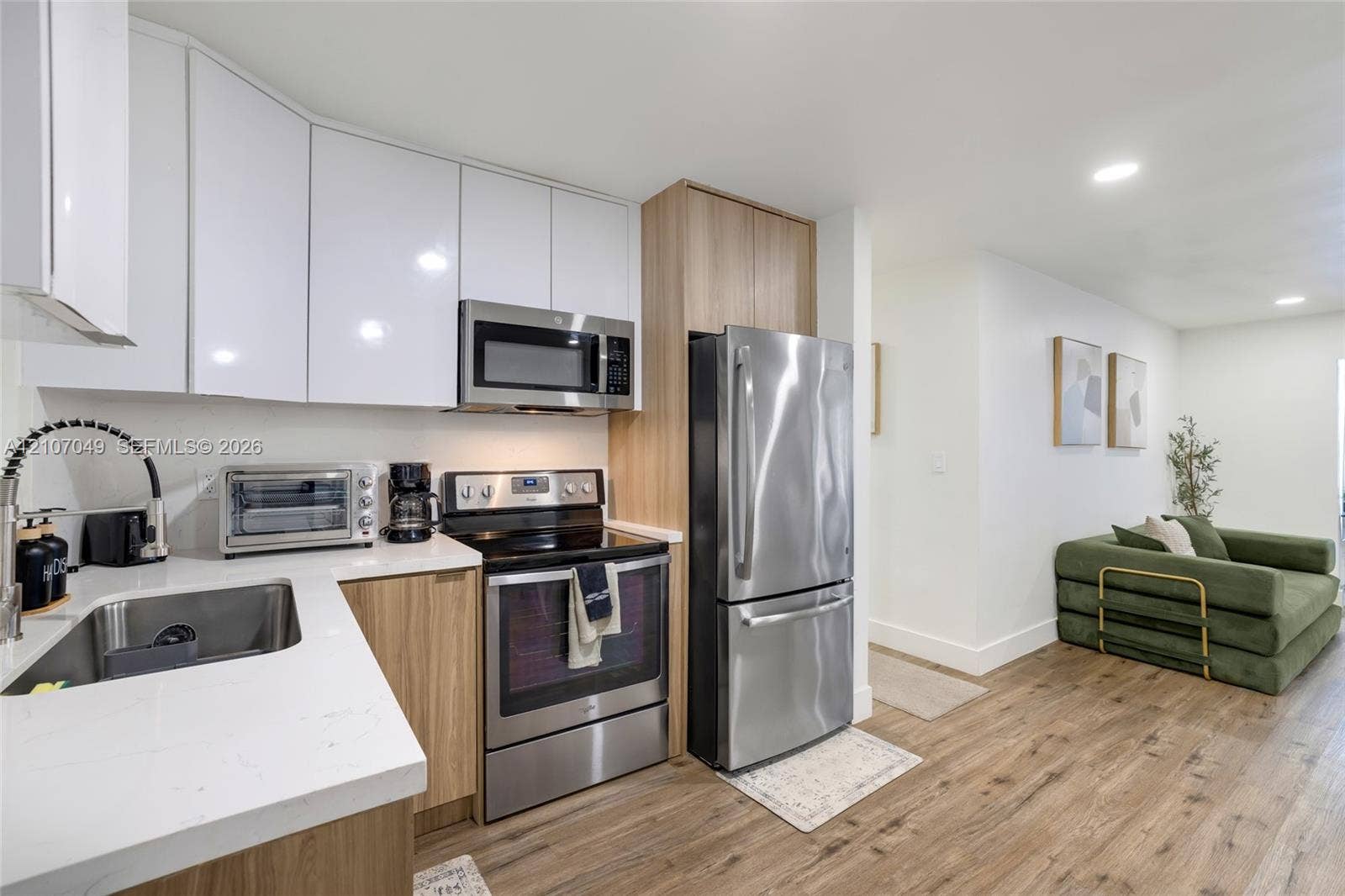 1009 NE 18th Street, Fort Lauderdale, FL 33305 Kitchen featuring white upper cabinetry, wood-finish lower cabinetry, quartz countertops, stainless steel appliances, and wood-finish flooring