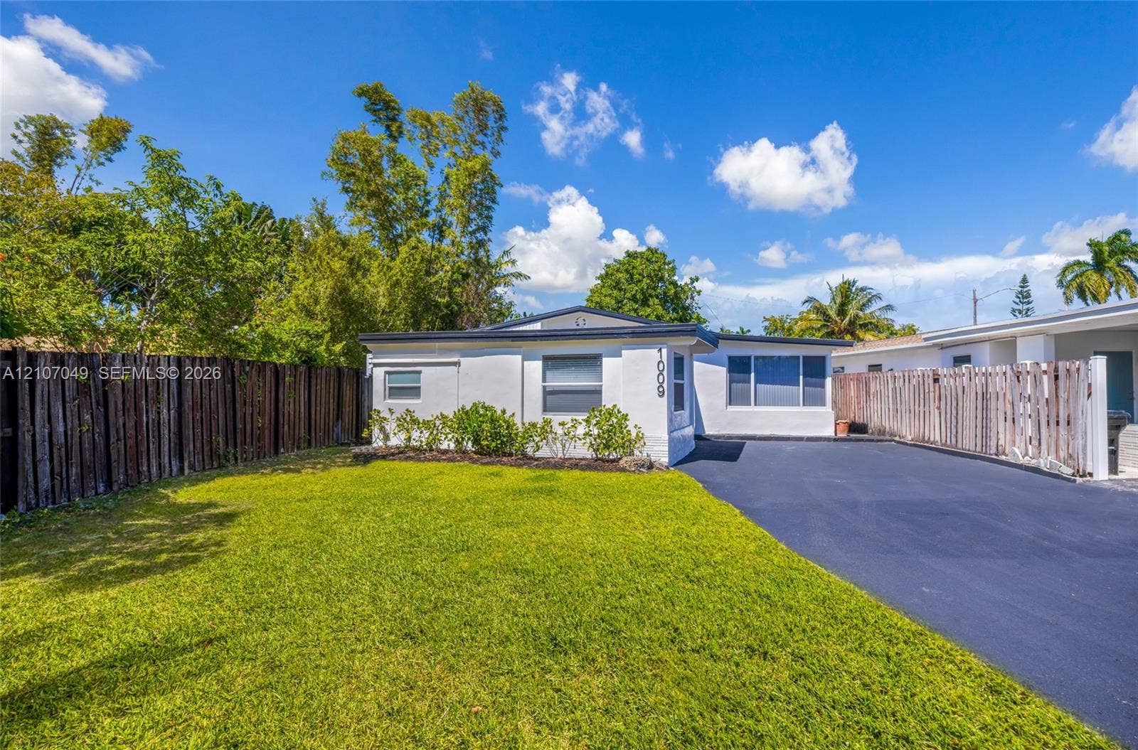 1009 NE 18th Street, Fort Lauderdale, FL 33305 Single-story residence featuring a white stucco exterior, asphalt driveway, horizontal wood fencing, and manicured lawn