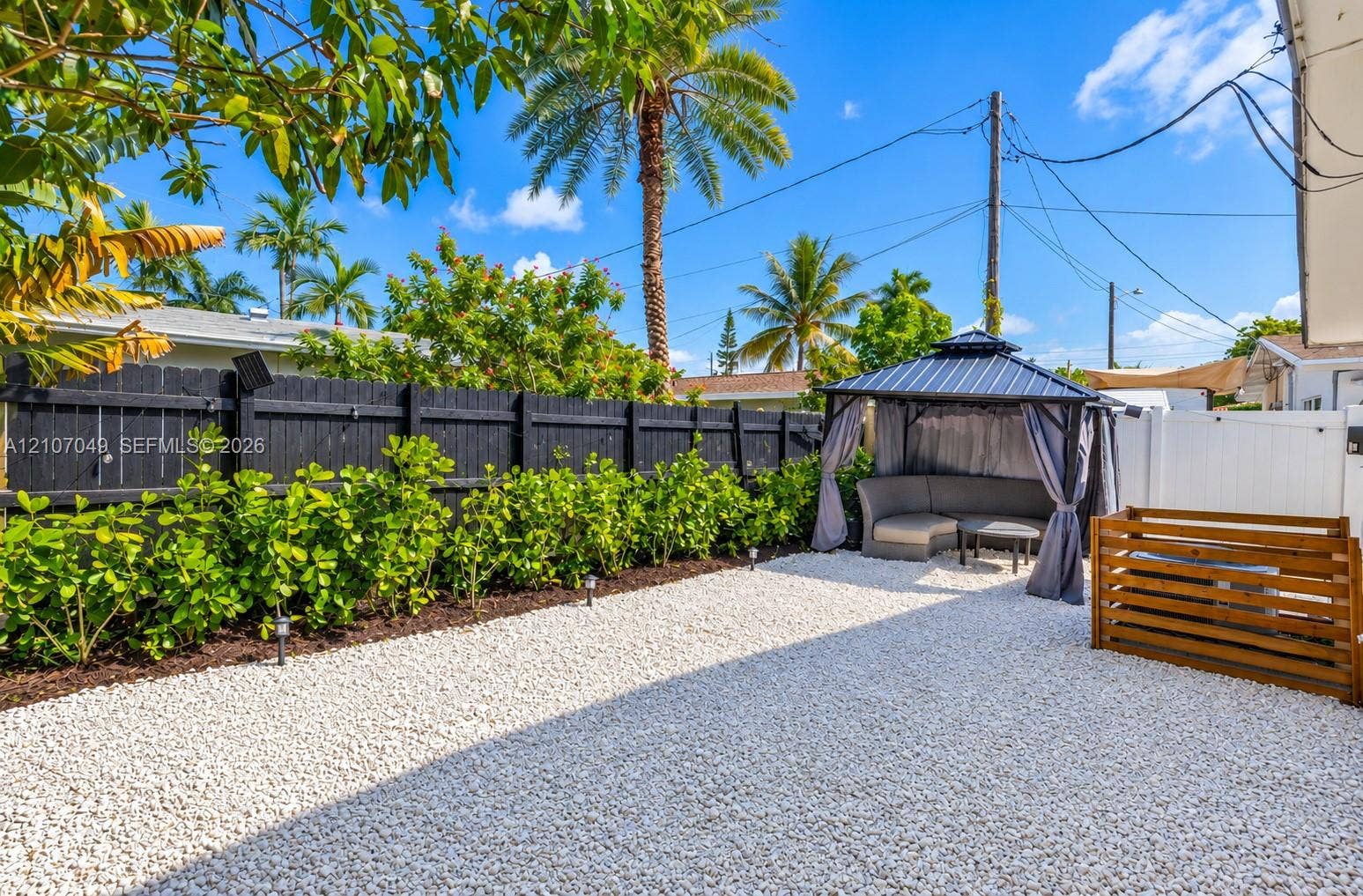 1009 NE 18th Street, Fort Lauderdale, FL 33305 Backyard featuring a white stone-covered ground, black-painted wood privacy fencing, a manicured hedge border, and a wood-slat enclosure