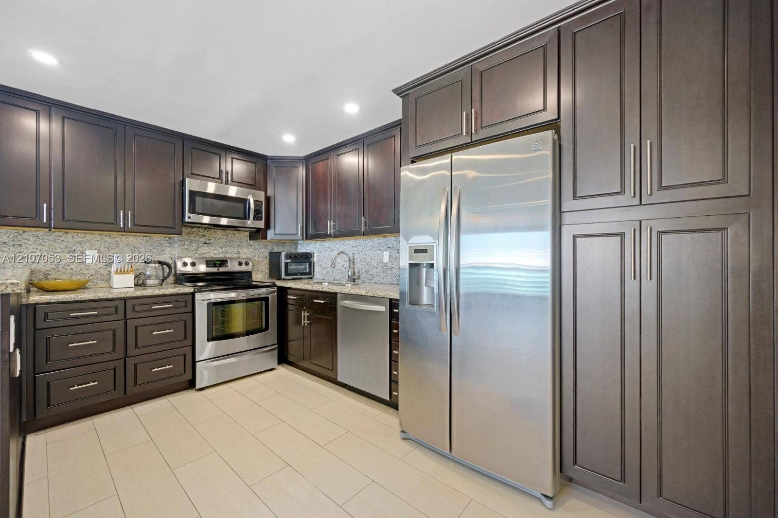 19370 Collins Avenue, #1403, Sunny Isles Beach, FL 33160 Kitchen featuring dark wood cabinetry, stainless steel appliances, stone-look countertops, tiled backsplash, and recessed lighting