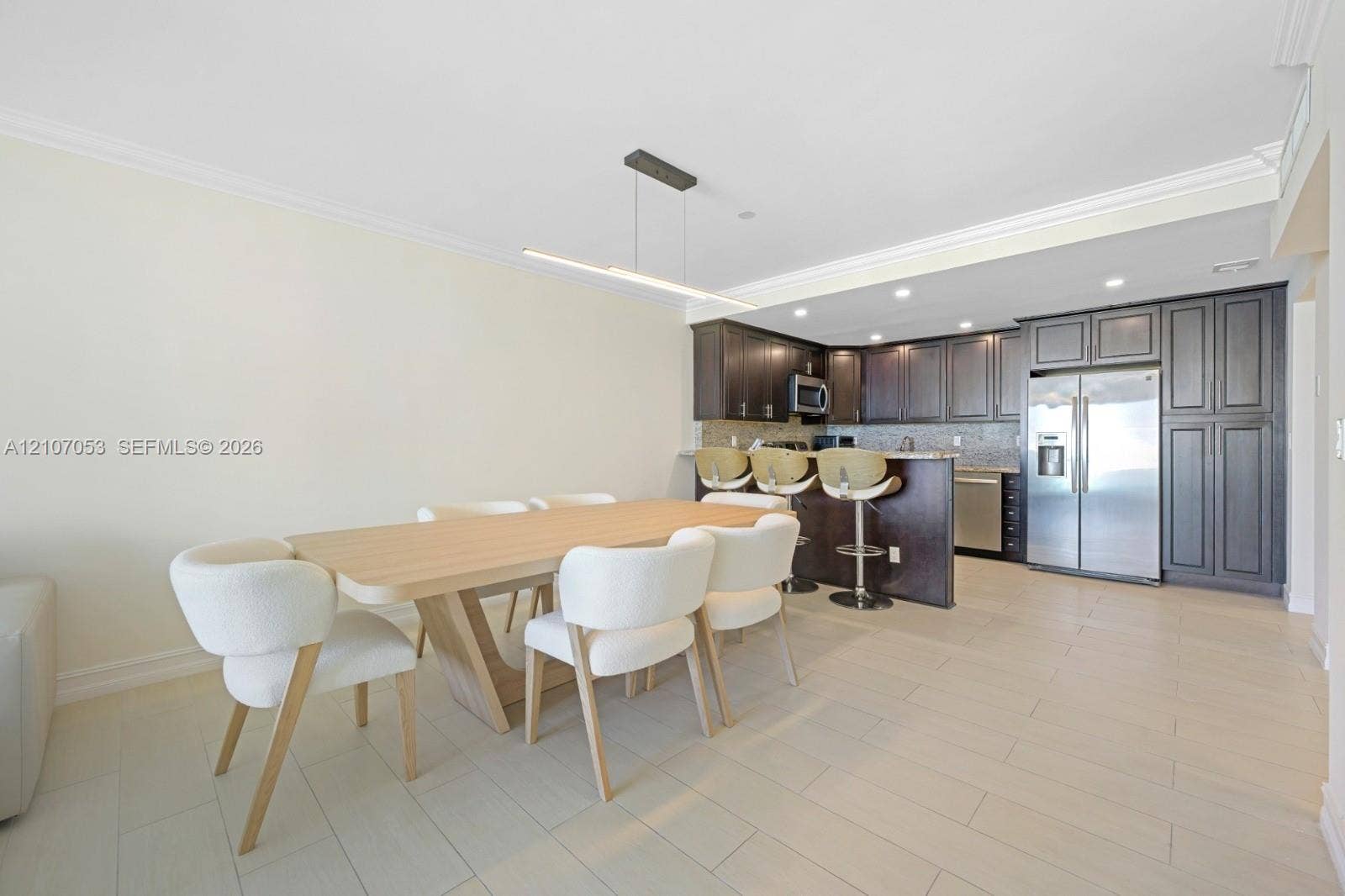 19370 Collins Avenue, #1403, Sunny Isles Beach, FL 33160 Open-concept kitchen featuring dark wood cabinetry, stainless steel appliances, neutral stone-finish countertops, tile flooring, and a modern linear pendant light fixture