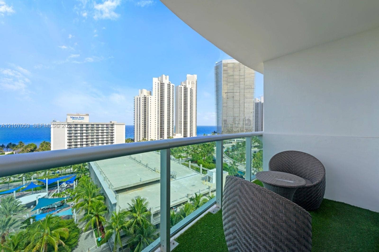 19370 Collins Avenue, #1403, Sunny Isles Beach, FL 33160 Covered balcony featuring a glass and metal railing, synthetic turf flooring, and horizon ocean and city skyline scenery