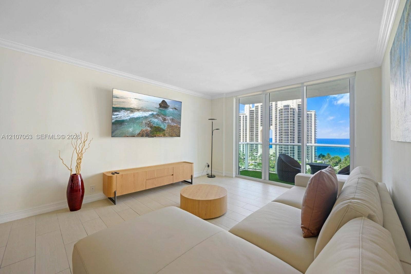 19370 Collins Avenue, #1403, Sunny Isles Beach, FL 33160 Living area featuring large-format tile flooring, crown molding, and floor-to-ceiling glass sliding doors opening to a balcony with ocean and cityscape scenery