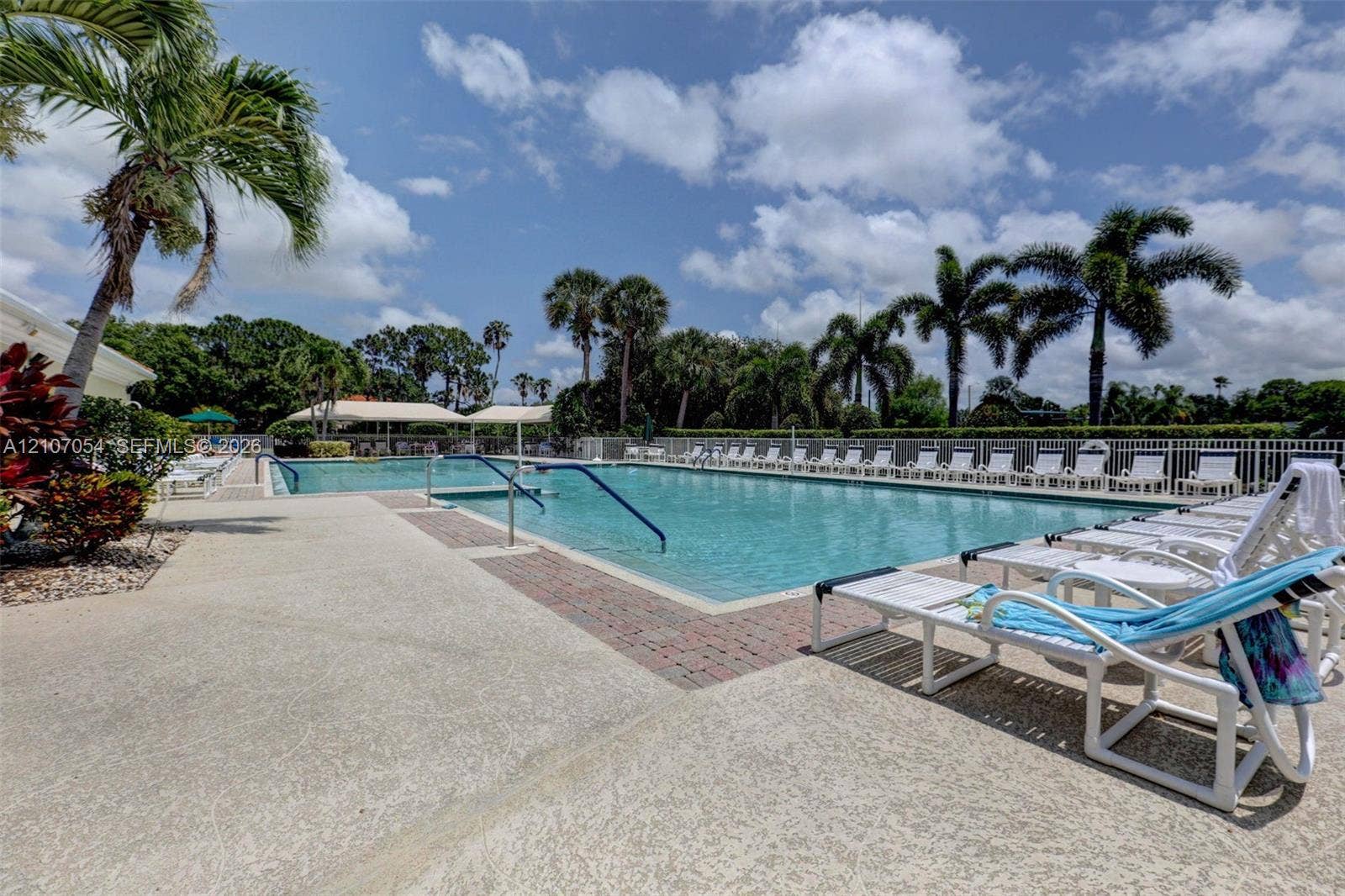 In-ground swimming pool featuring a brick-paver border, textured concrete decking, metal safety rails, and perimeter fencing