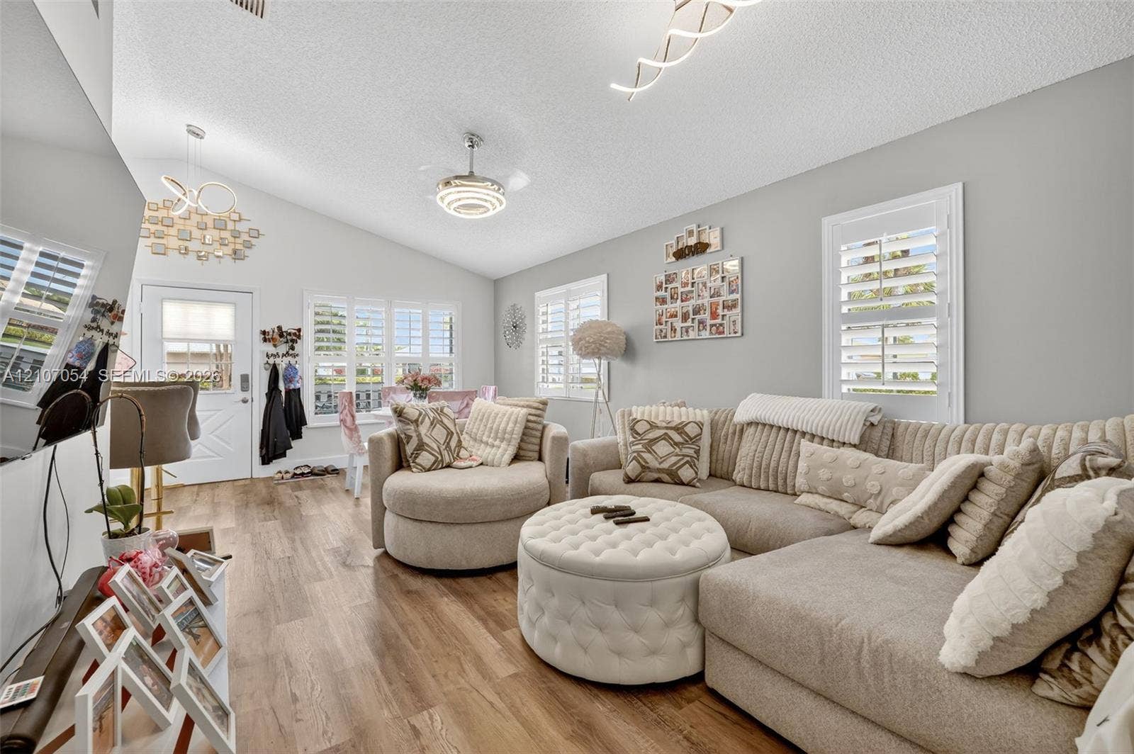 Living area featuring laminate flooring, vaulted ceilings, multi-light chandeliers, and windows outfitted with white plantation shutters