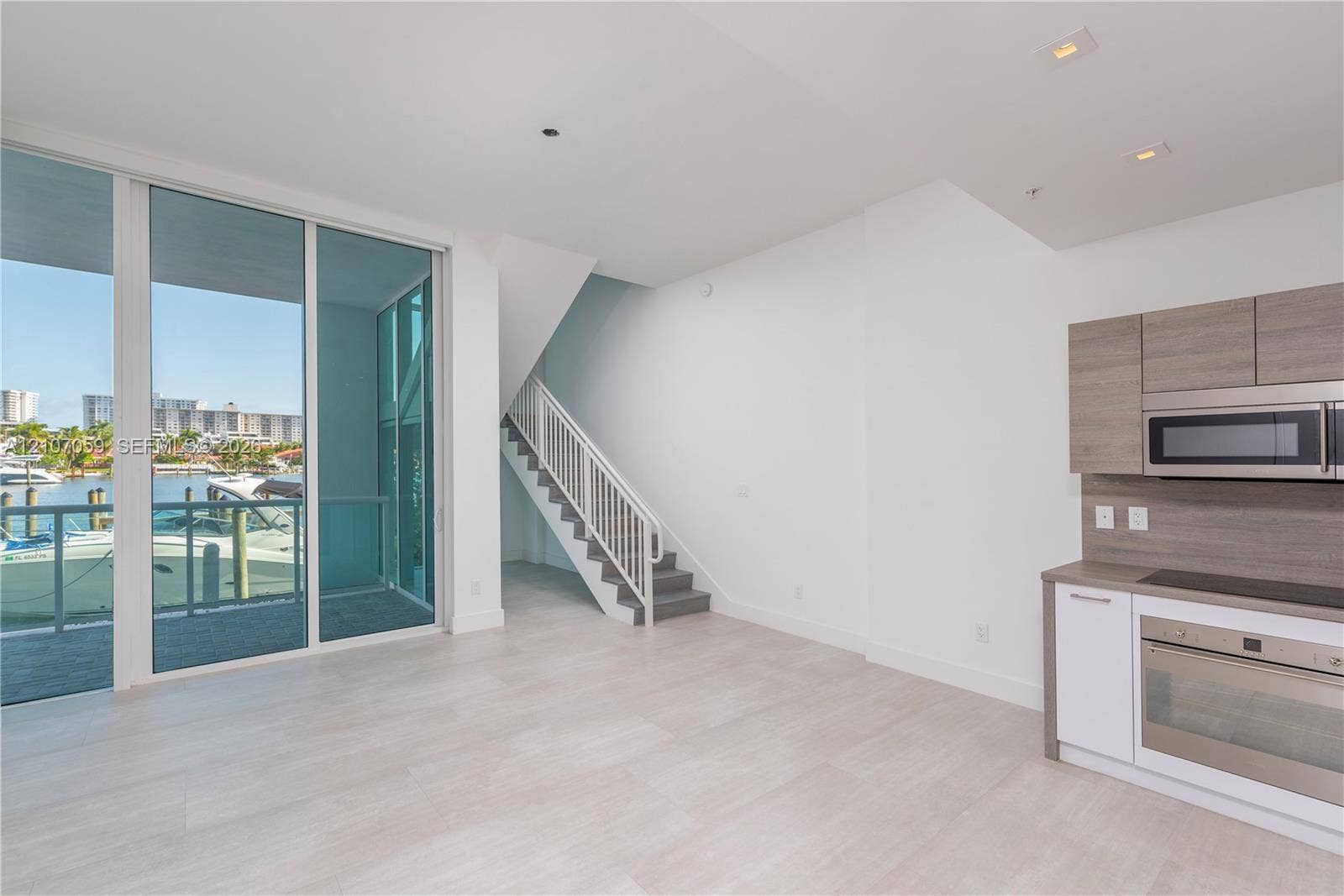 400 Sunny Isles Boulevard, #121, Sunny Isles Beach, FL 33160 Floor-to-ceiling glass sliding doors, wood-finish cabinetry, built-in stainless steel appliances, recessed ceiling lighting, and a staircase with a metal railing