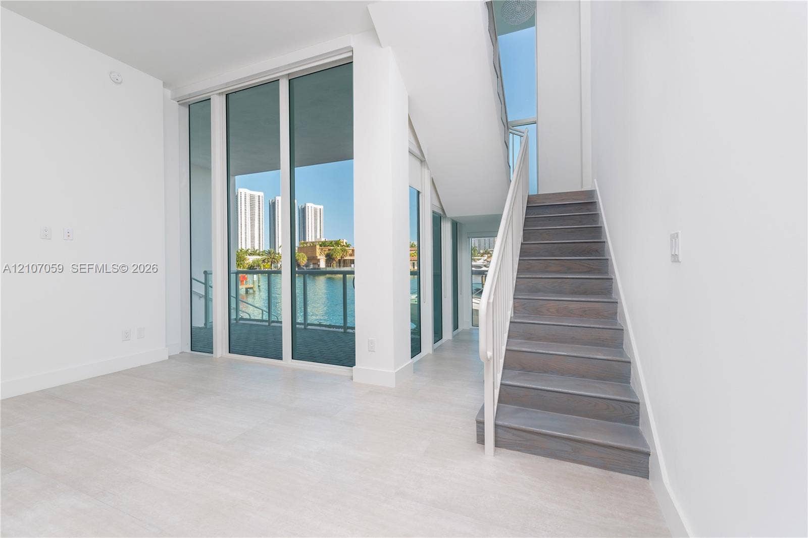 400 Sunny Isles Boulevard, #121, Sunny Isles Beach, FL 33160 Double-height ceilings with floor-to-ceiling glass panels, large-format tile flooring, a staircase featuring wood-finish treads, and a metal handrail