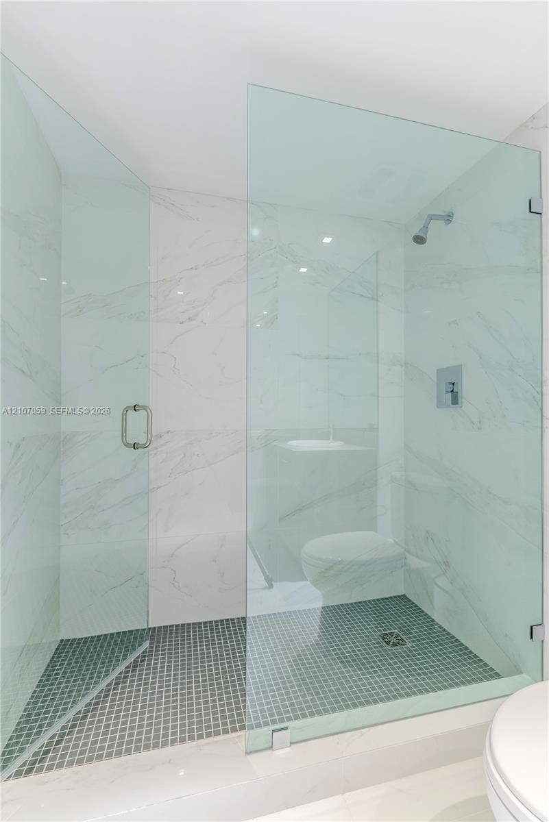 400 Sunny Isles Boulevard, #121, Sunny Isles Beach, FL 33160 Walk-in shower featuring a frameless glass enclosure, floor-to-ceiling stone-style wall tile, dark mosaic tile flooring, and a wall-mounted shower head