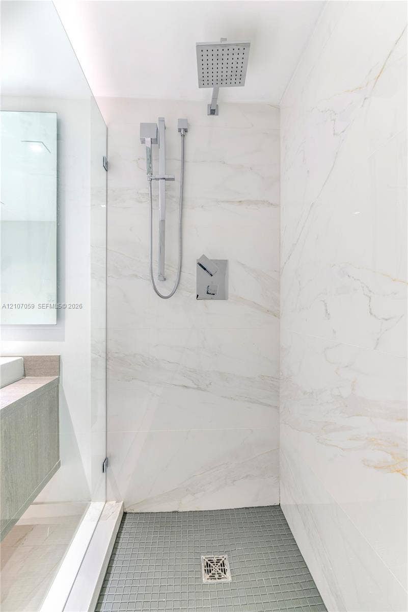 400 Sunny Isles Boulevard, #121, Sunny Isles Beach, FL 33160 Walk-in shower featuring large-format stone wall tiling, a rainfall showerhead, a separate handheld sprayer, a glass enclosure, and a mosaic-tiled floor