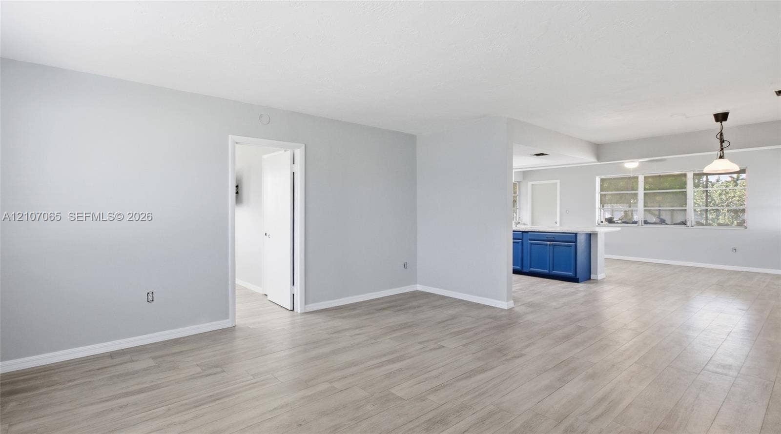 Open floor plan featuring wood-finish flooring, neutral wall paint, multi-pane windows, and a peninsula-style kitchen counter with blue cabinetry