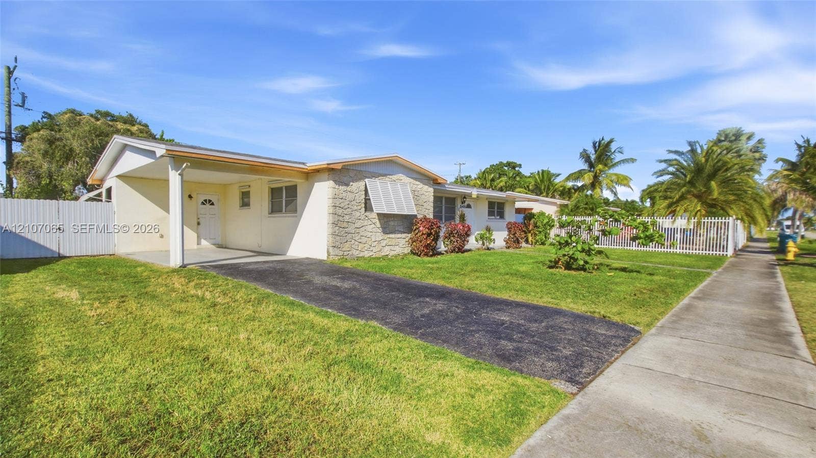 Single-story residence featuring a covered carport, stone facade detailing, and a white privacy fence encompassing the property grounds