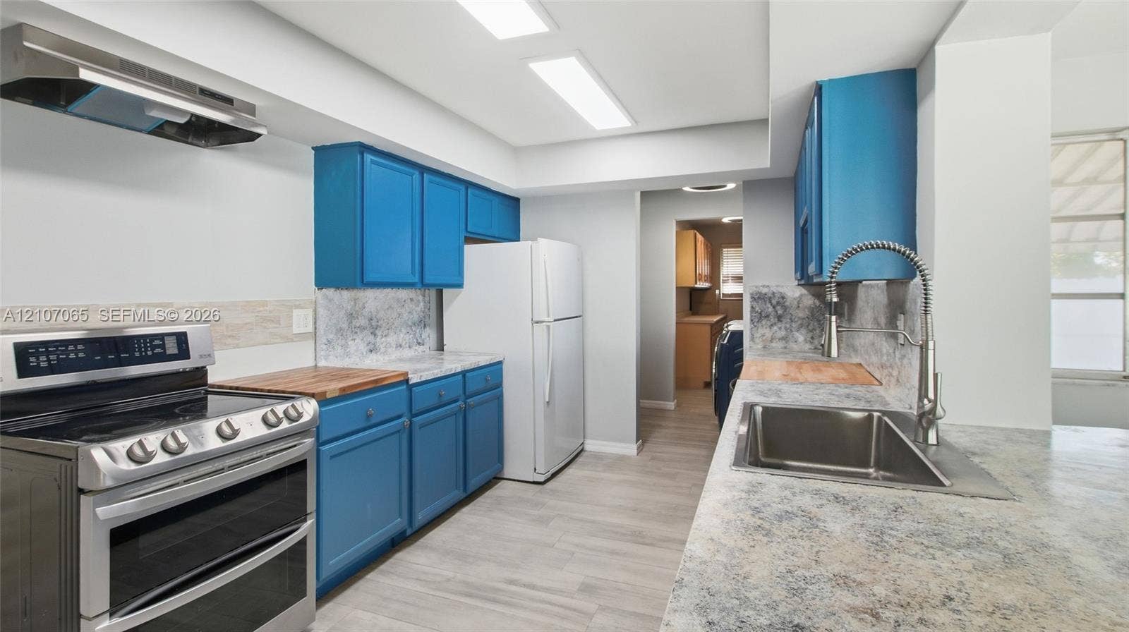 Kitchen featuring stone-patterned countertops, stainless steel range with overhead vent hood, under-mount stainless steel sink with high-arc pull-down faucet, and wood-finish flooring