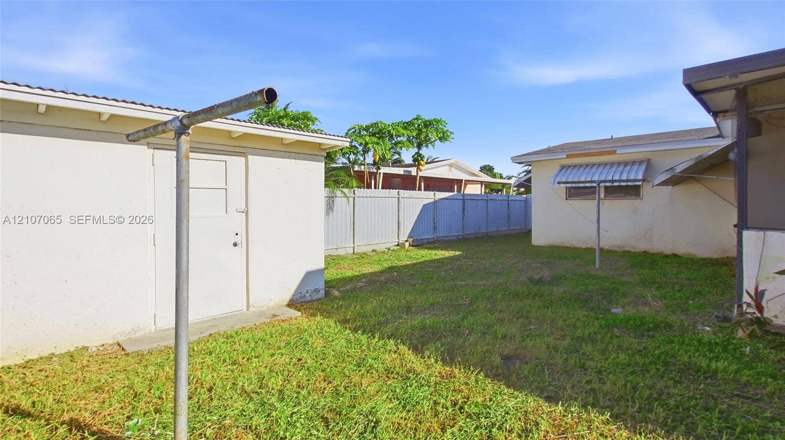 Exterior space featuring a grass yard, perimeter metal fencing, and an attached storage structure