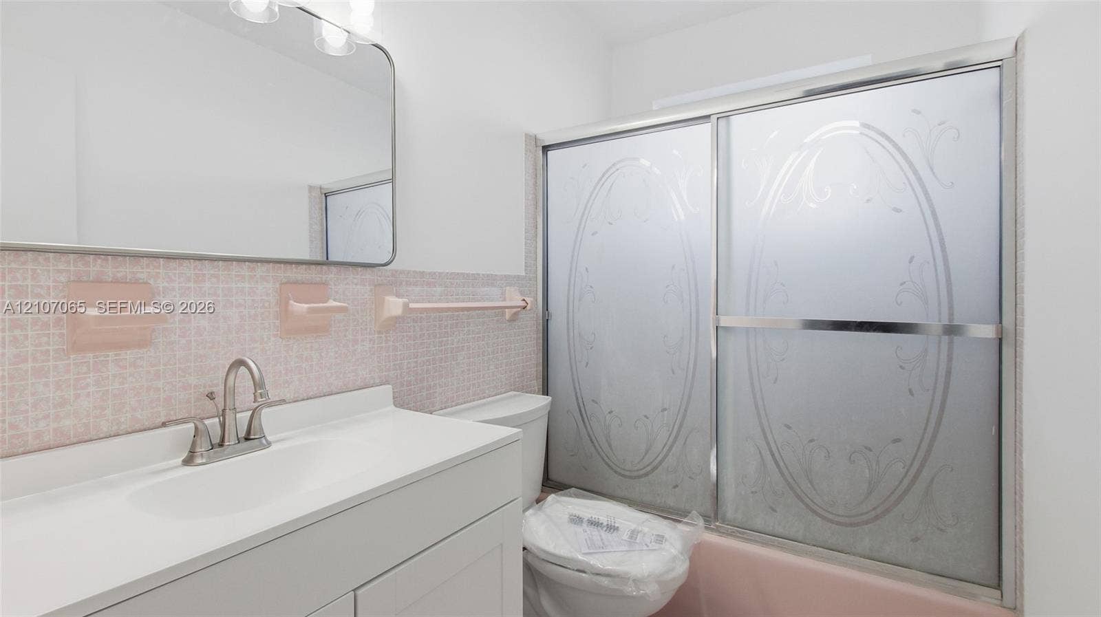 Bathroom featuring a solid-surface countertop, integrated basin, wall-mounted mirror, and a shower-tub combination with etched sliding glass doors and decorative mosaic tile backsplash
