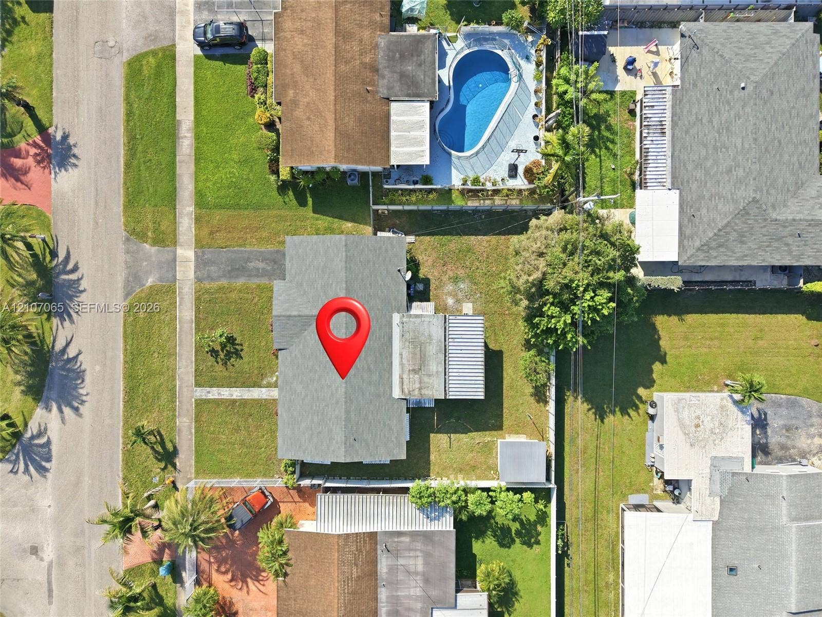 Aerial perspective of a property featuring a rectangular lot, a pitched roofline, paved driveway, and established landscaping
